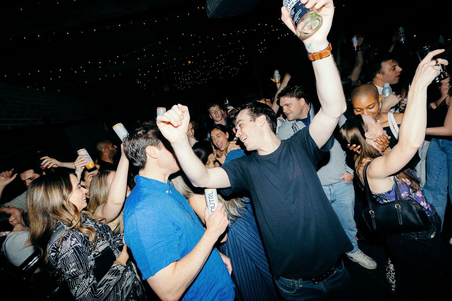 A crowd of people enjoying themselves dancing together at a nightclub or party in dim lighting.