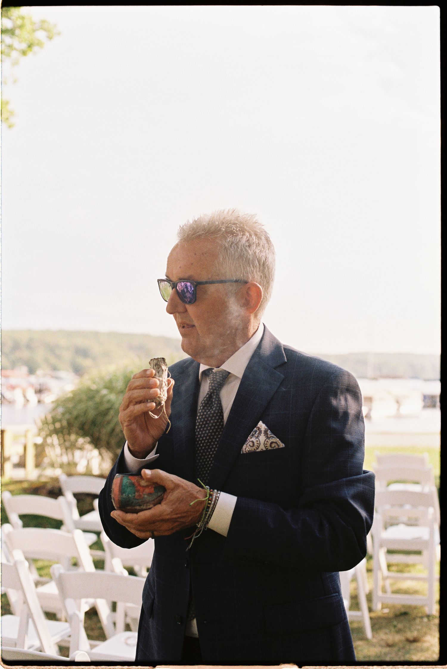 Elegant older wedding guest in navy suit and sunglasses at outdoor ceremony.