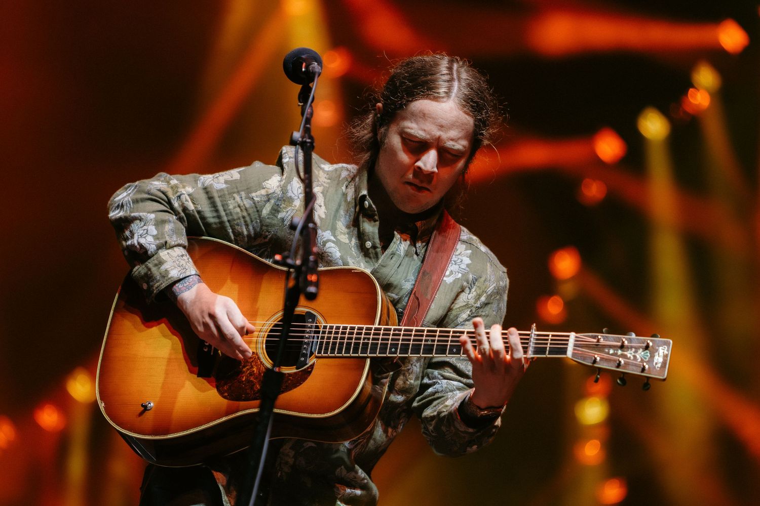 Musician performs on acoustic guitar under warm orange stage lighting during an intimate concert performance.