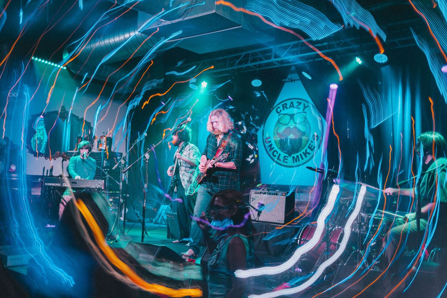 Band performing in venue with fisheye lens effect and blue lighting creating tunnel-like perspective.