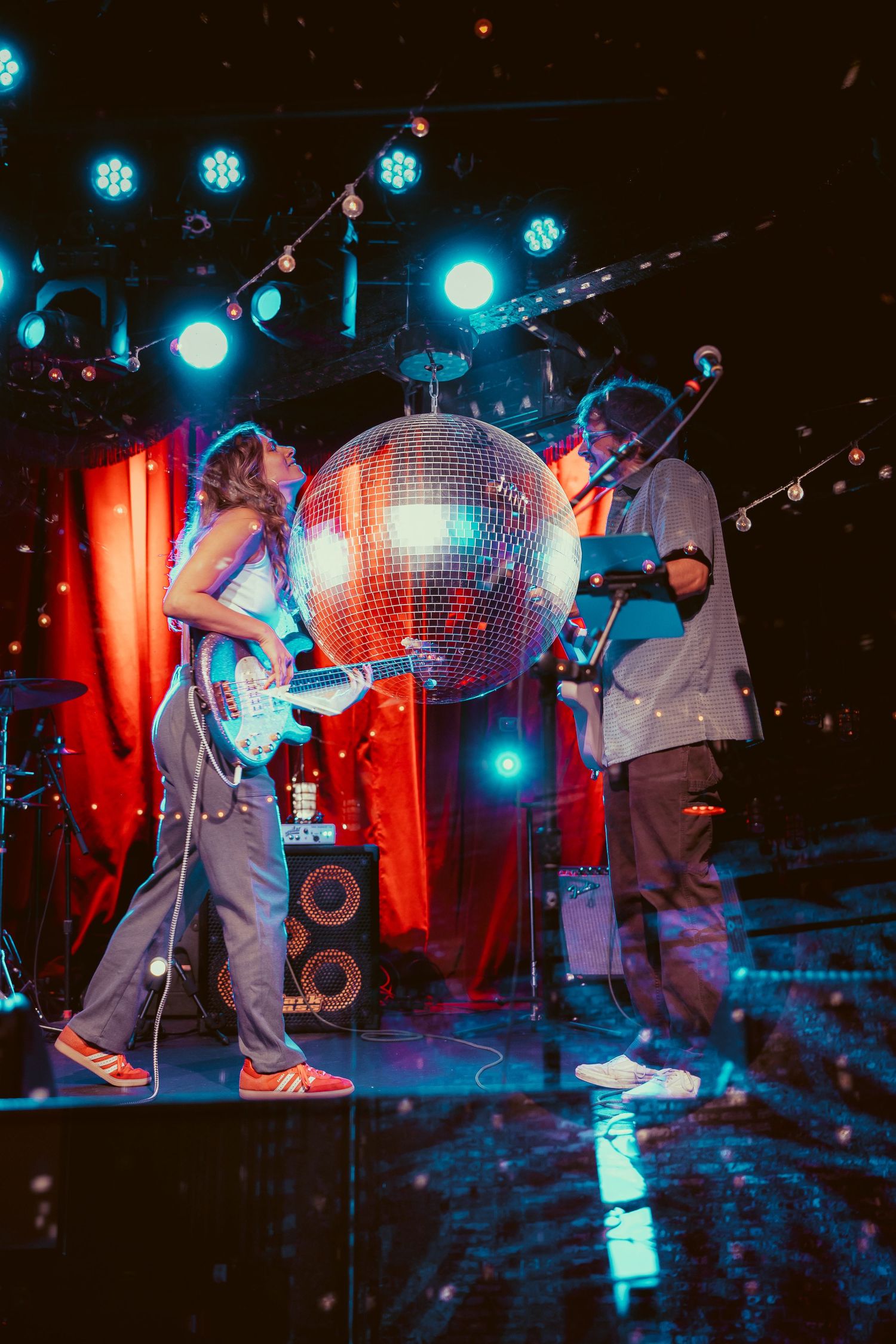 Musicians perform on stage with disco ball and dramatic blue and red lighting creating an atmospheric nightclub scene.