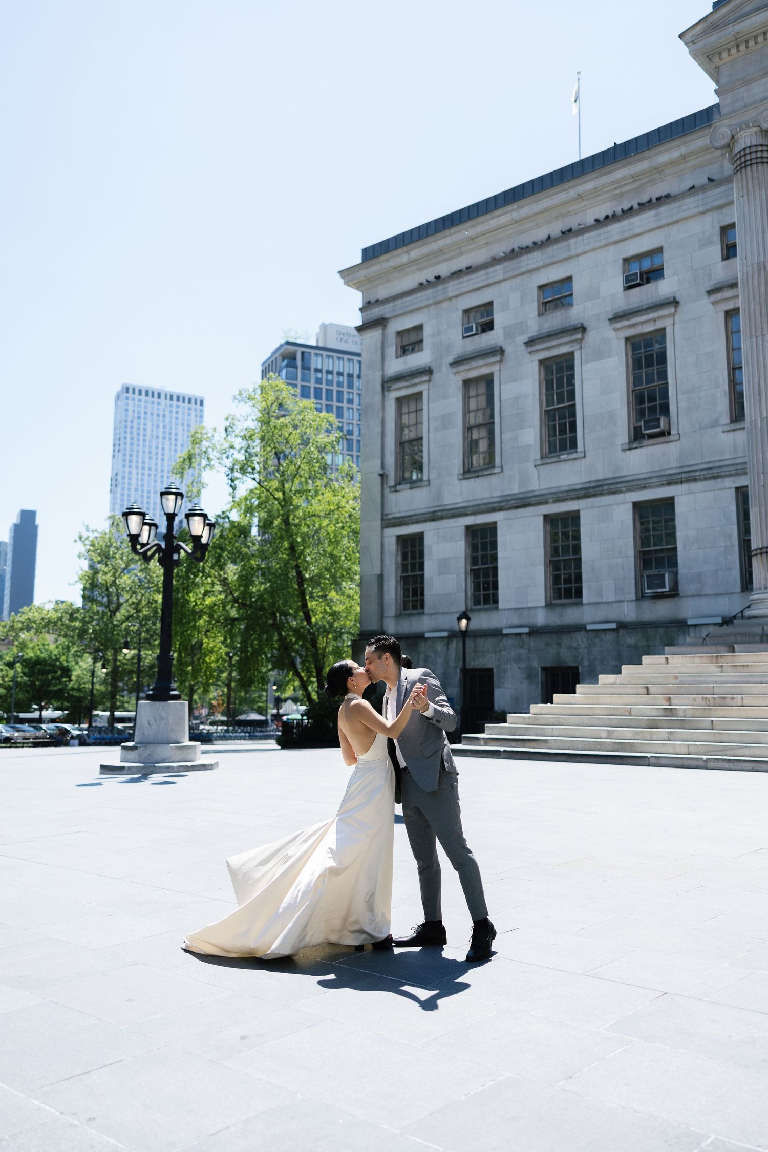 Bride and groom share a romantic kiss outside a grand neoclassical building on their sunny wedding day.
