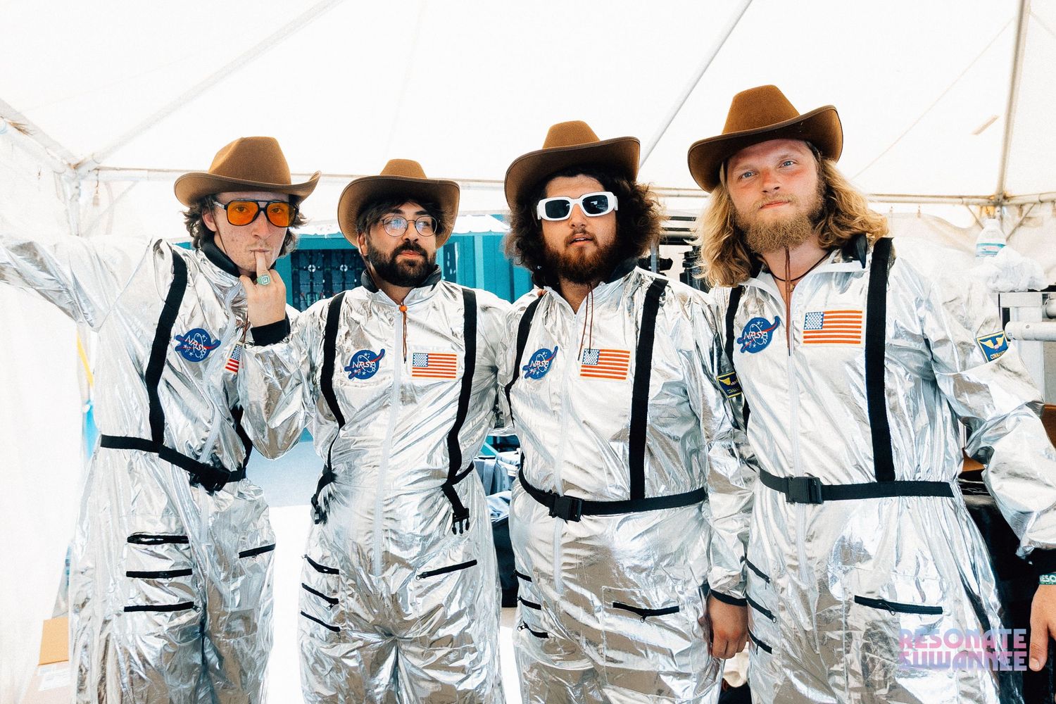 A group of astronauts in white NASA spacesuits with brown cowboy hats pose together outdoors.