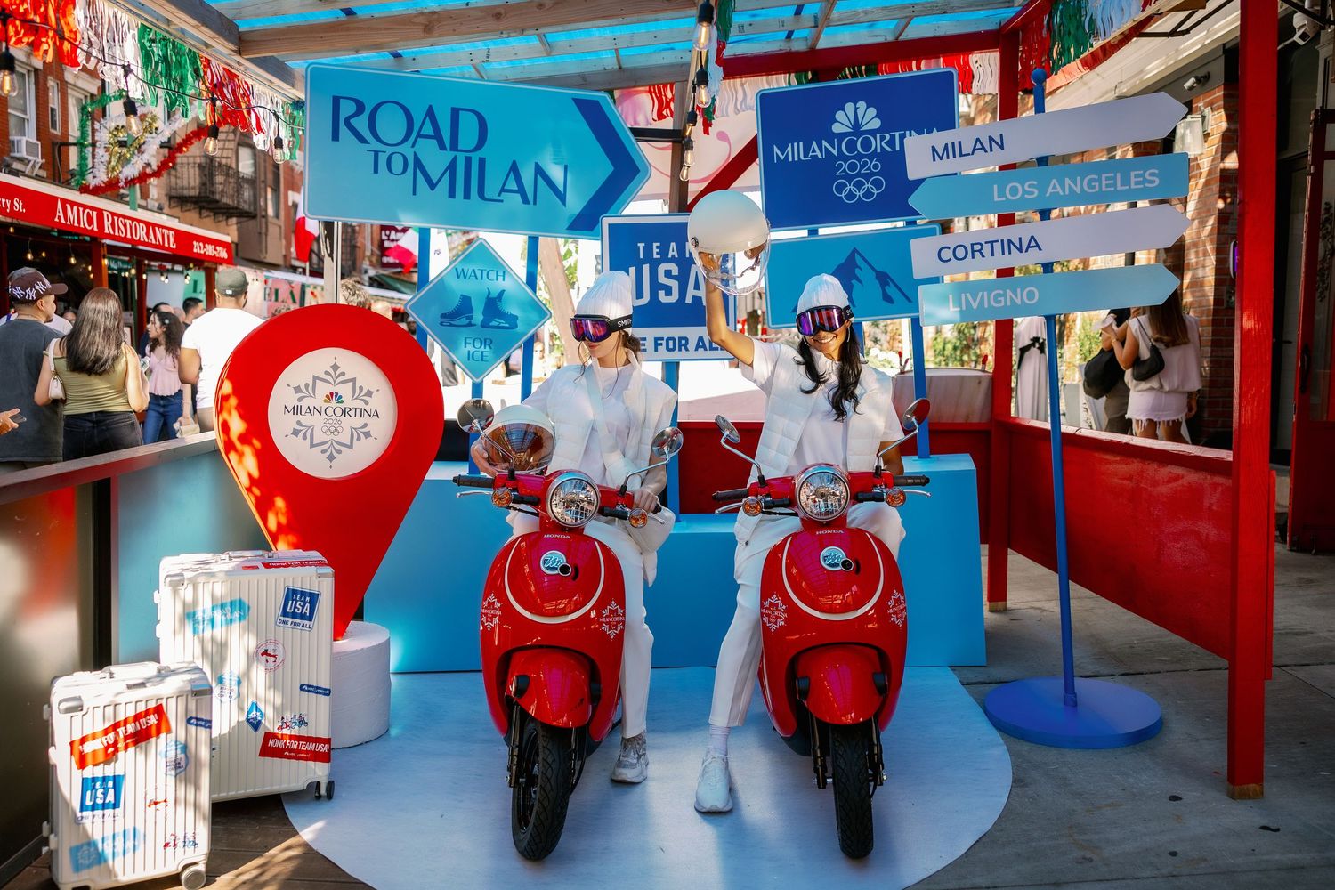 Red scooters on display at a promotional booth with blue and white decor and marketing banners in a retail setting.