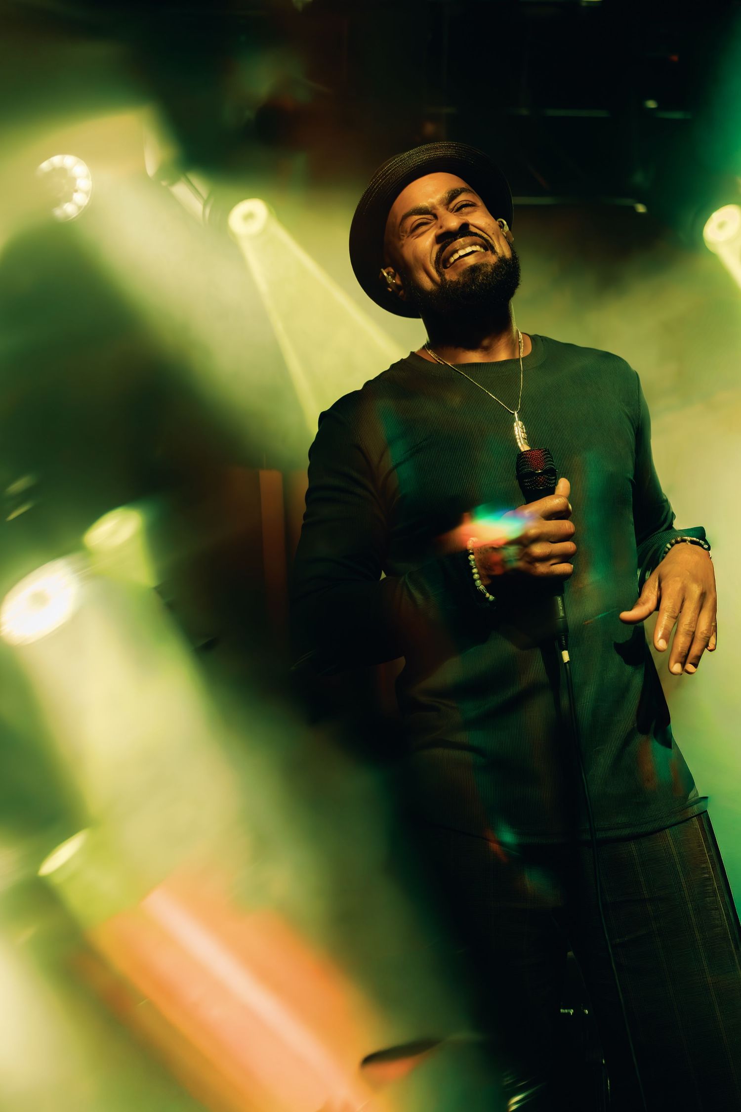 Singer in black hat performs on stage under green spotlights holding microphone.