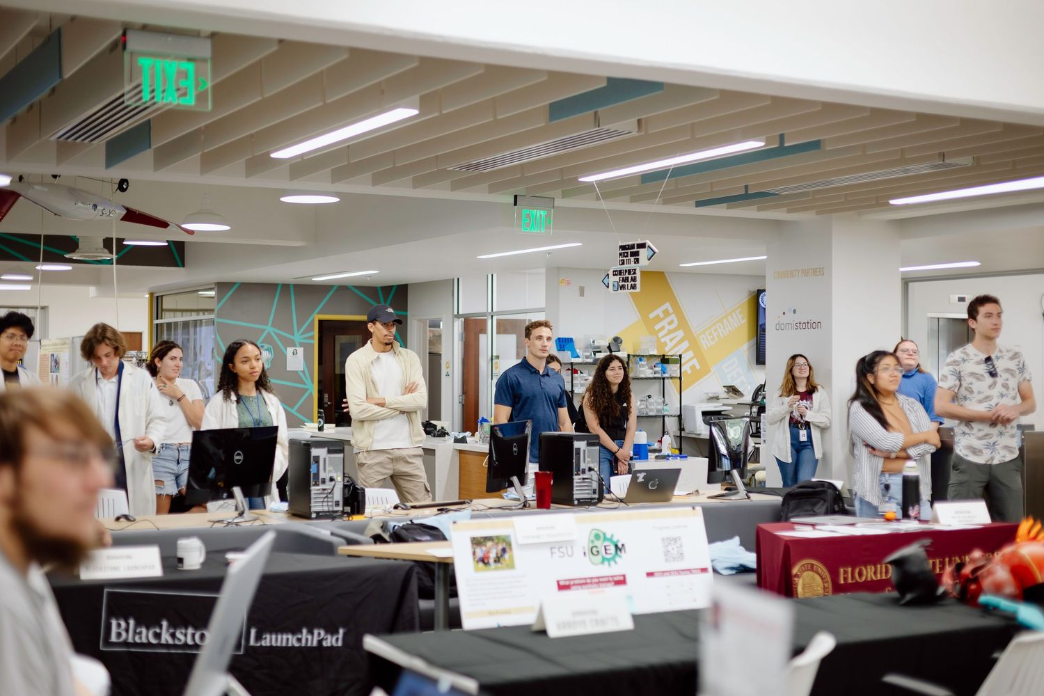 A group of people stand and observe during a workshop or meeting in a modern office space.