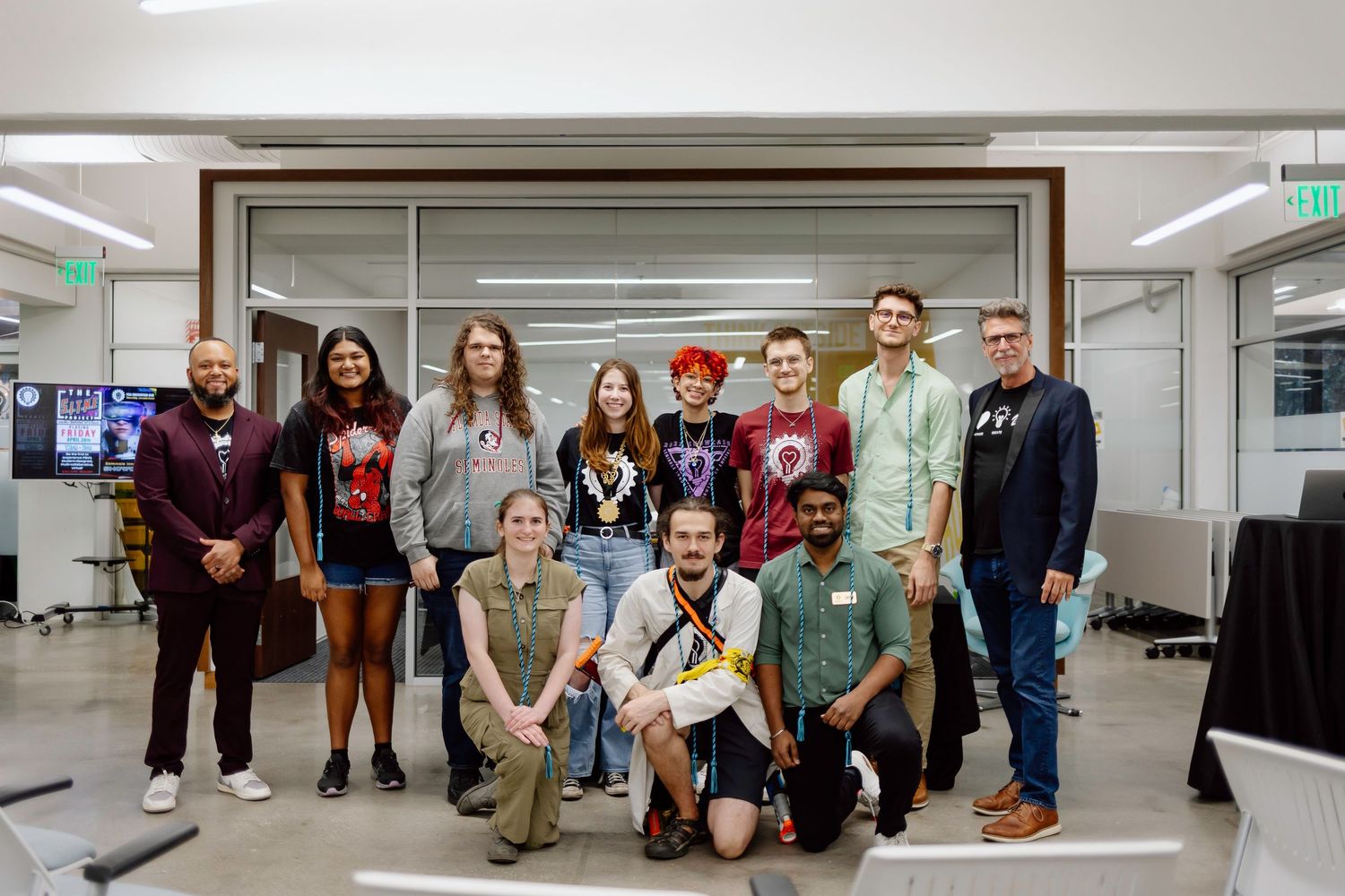 A diverse group of people pose together for a group photo in an indoor hallway setting.