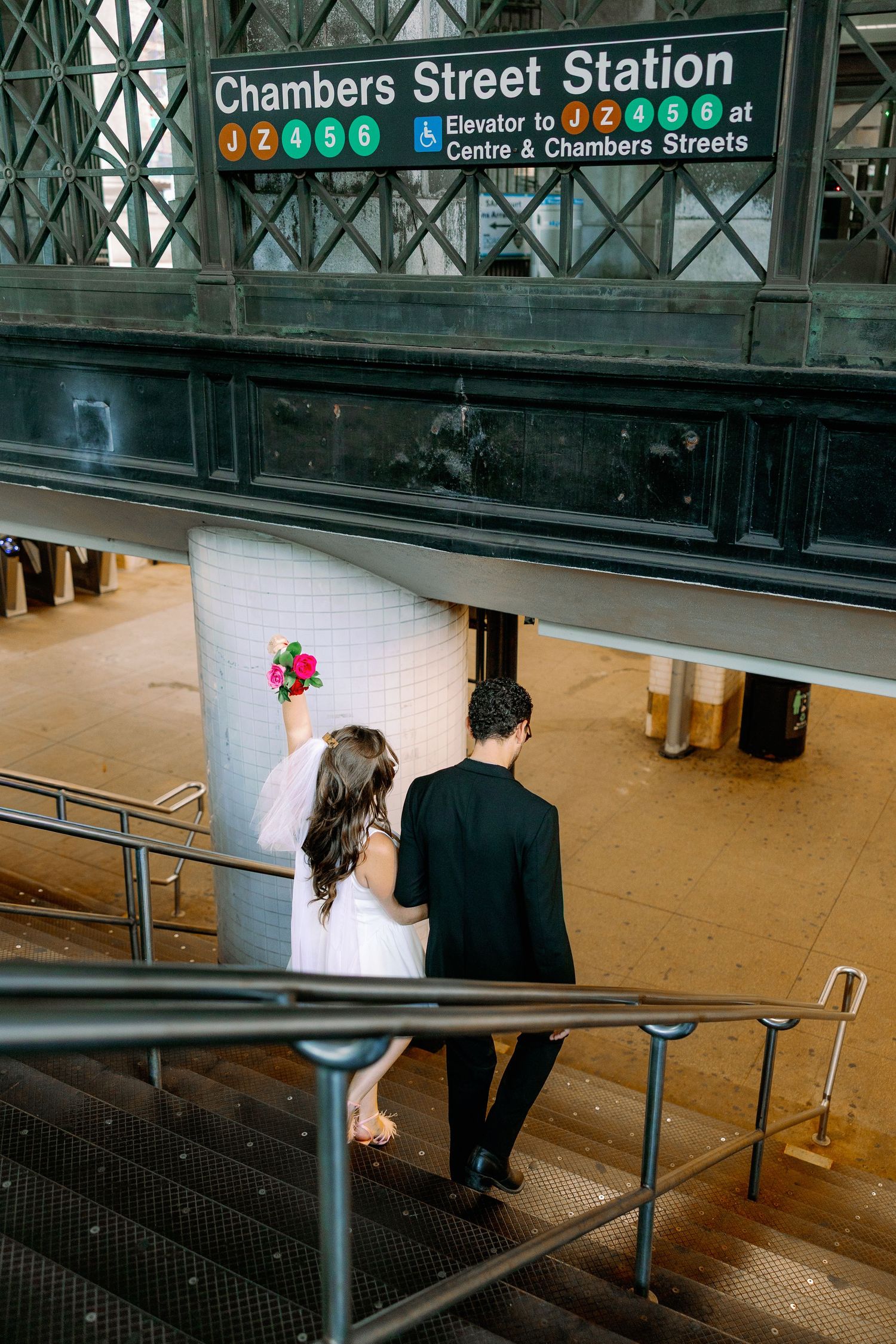 Couple descending stairs at Chambers Street subway station in New York City with colorful transit sign above.