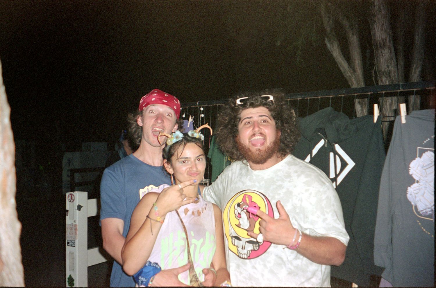 Three people posing together at a casual gathering with drinks and party accessories.