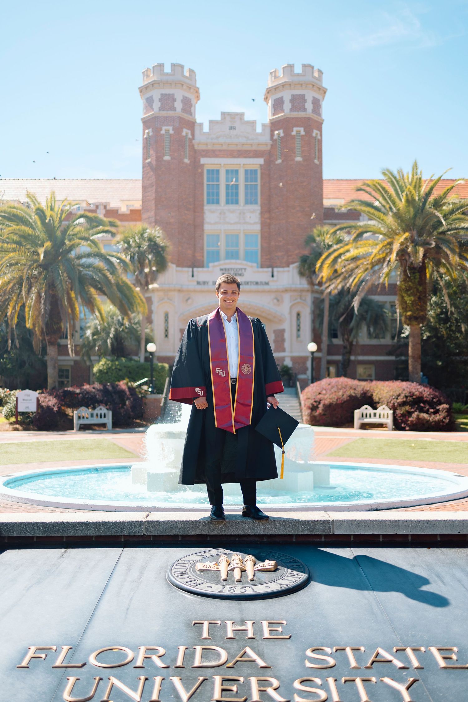 FSU Graduate in cap and gown poses in front of iconic FSU Westcott building and fountain.
