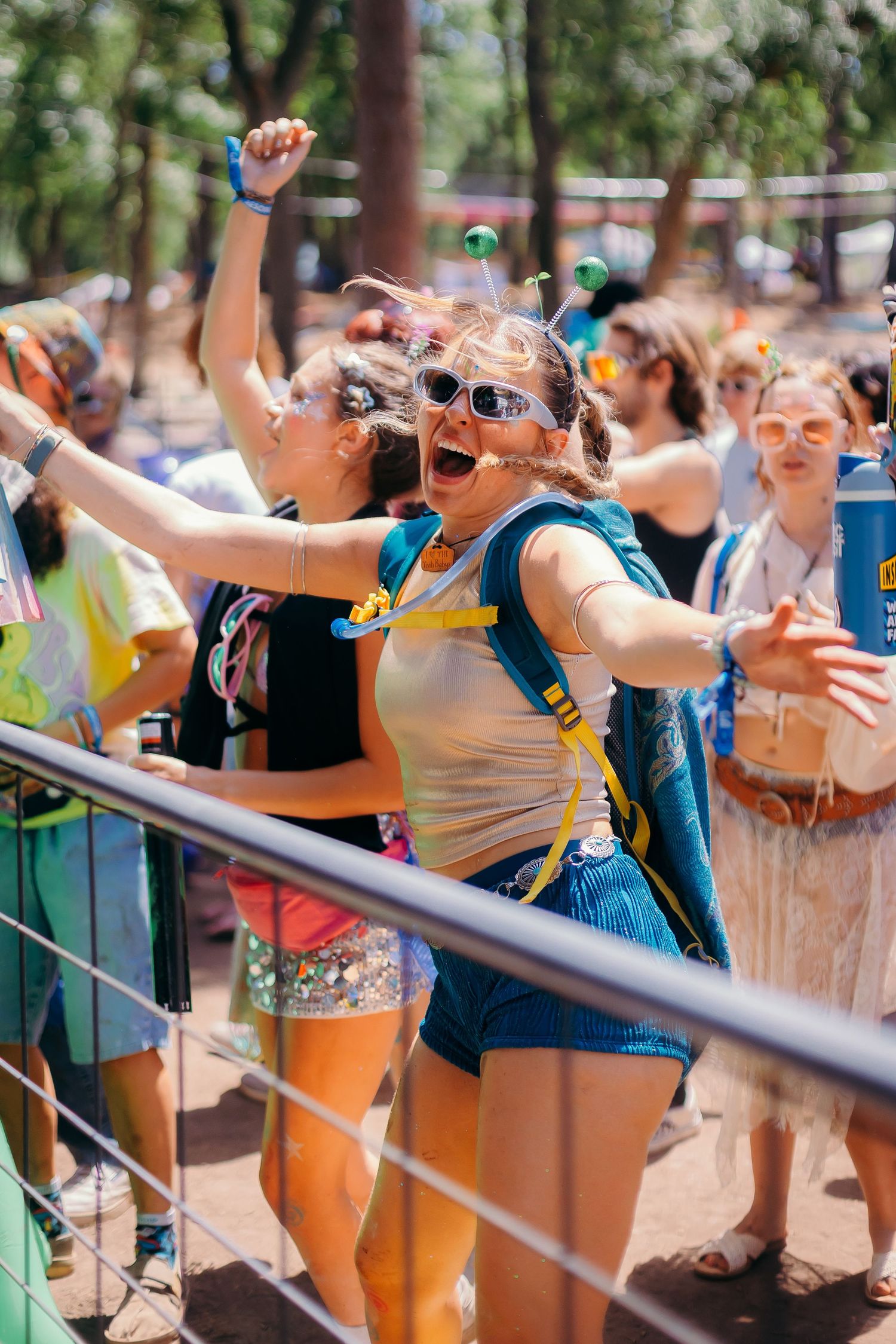 Enthusiastic crowd of festival attendees leaning over railings with arms outstretched at an outdoor summer event.