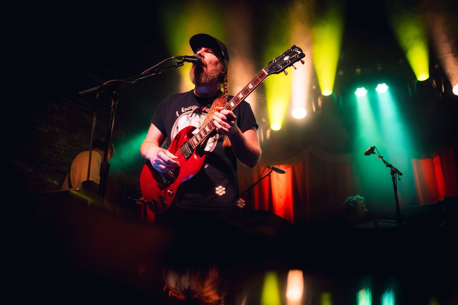 Silhouetted musicians perform on stage with vibrant red and green lighting creating a dramatic concert atmosphere.