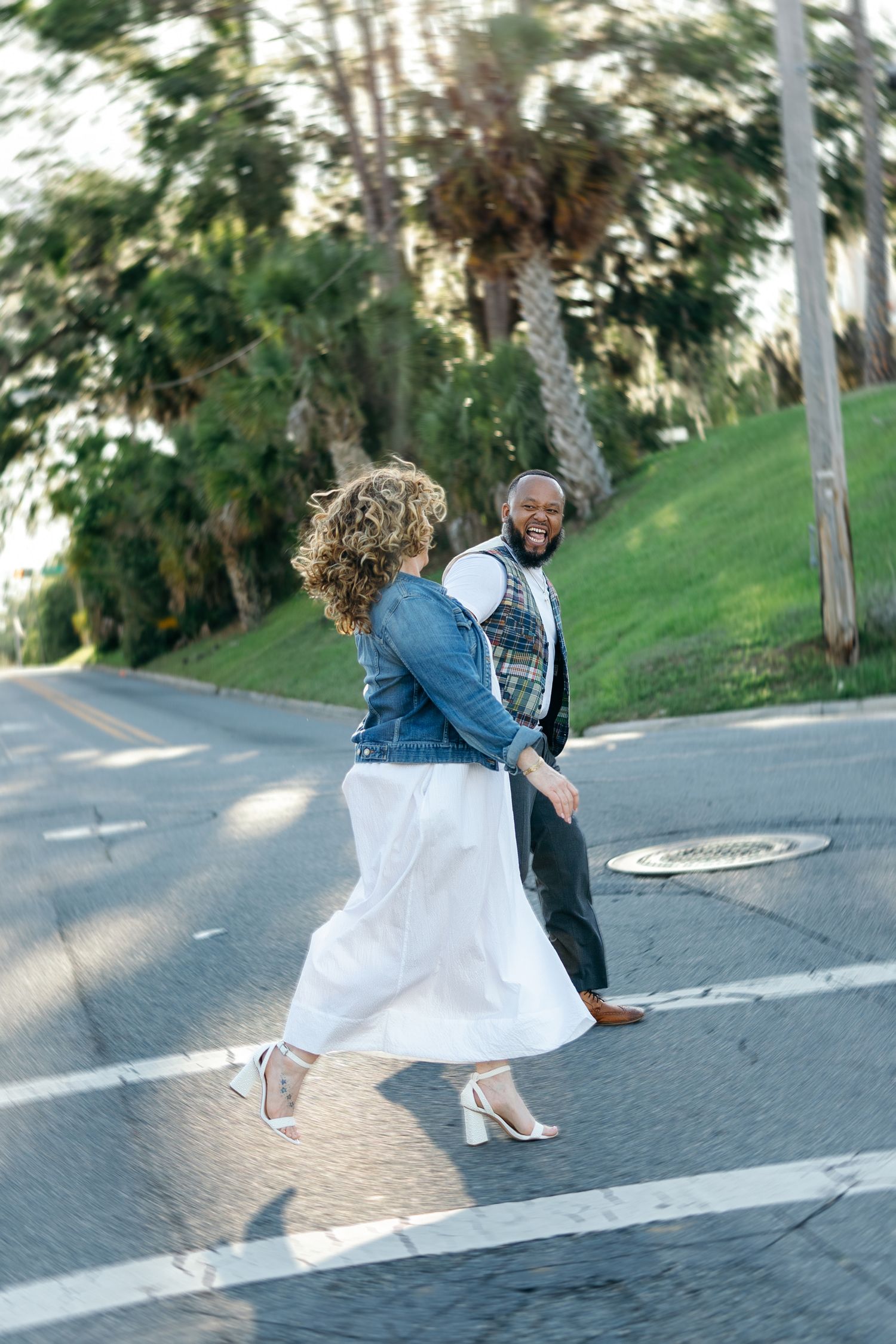 A couple dancing together on a quiet street with tall eucalyptus trees in the background on a sunny day.