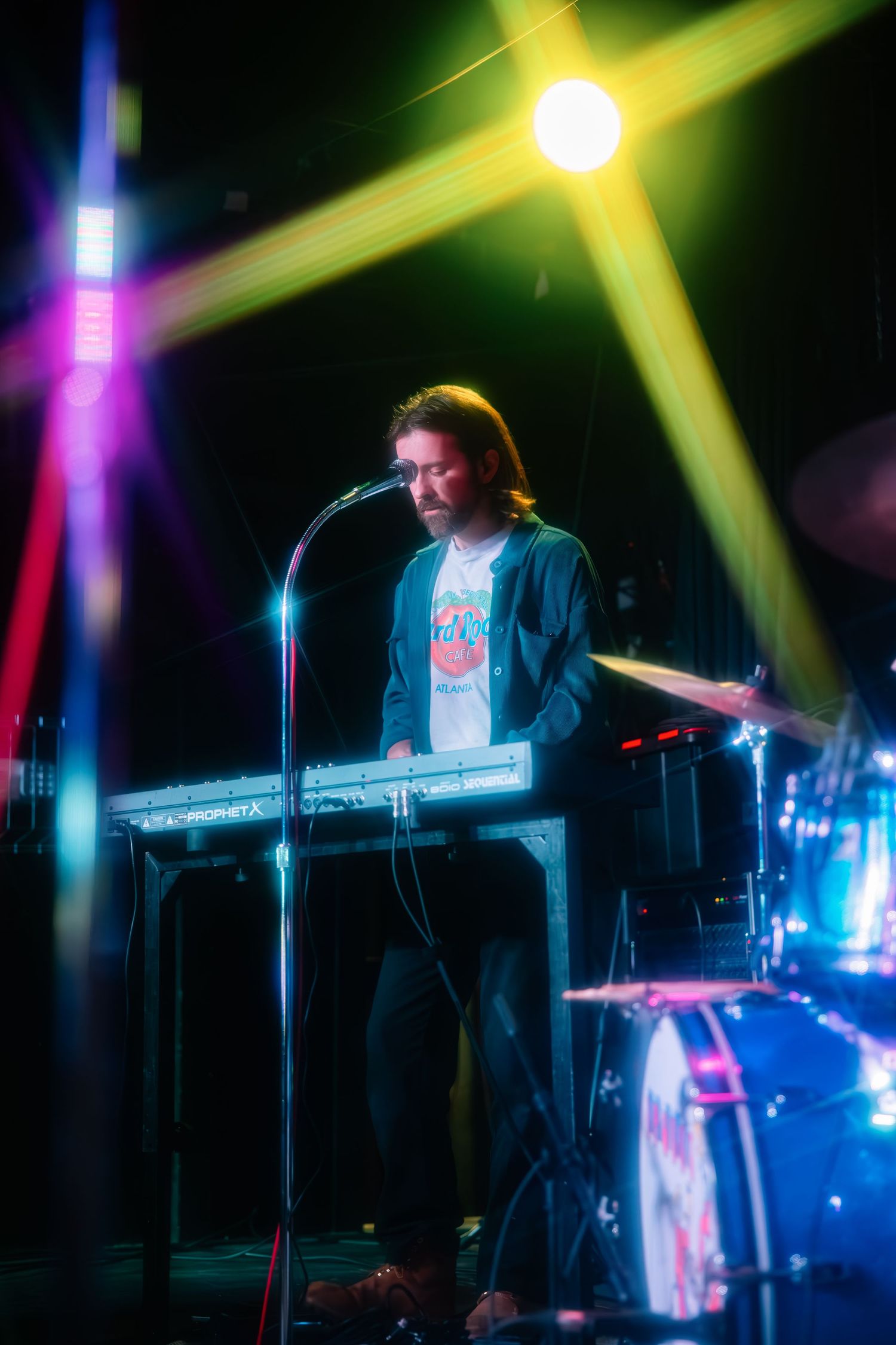 Concert performer illuminated by vibrant yellow and blue stage lights plays electronic keyboard during live show.