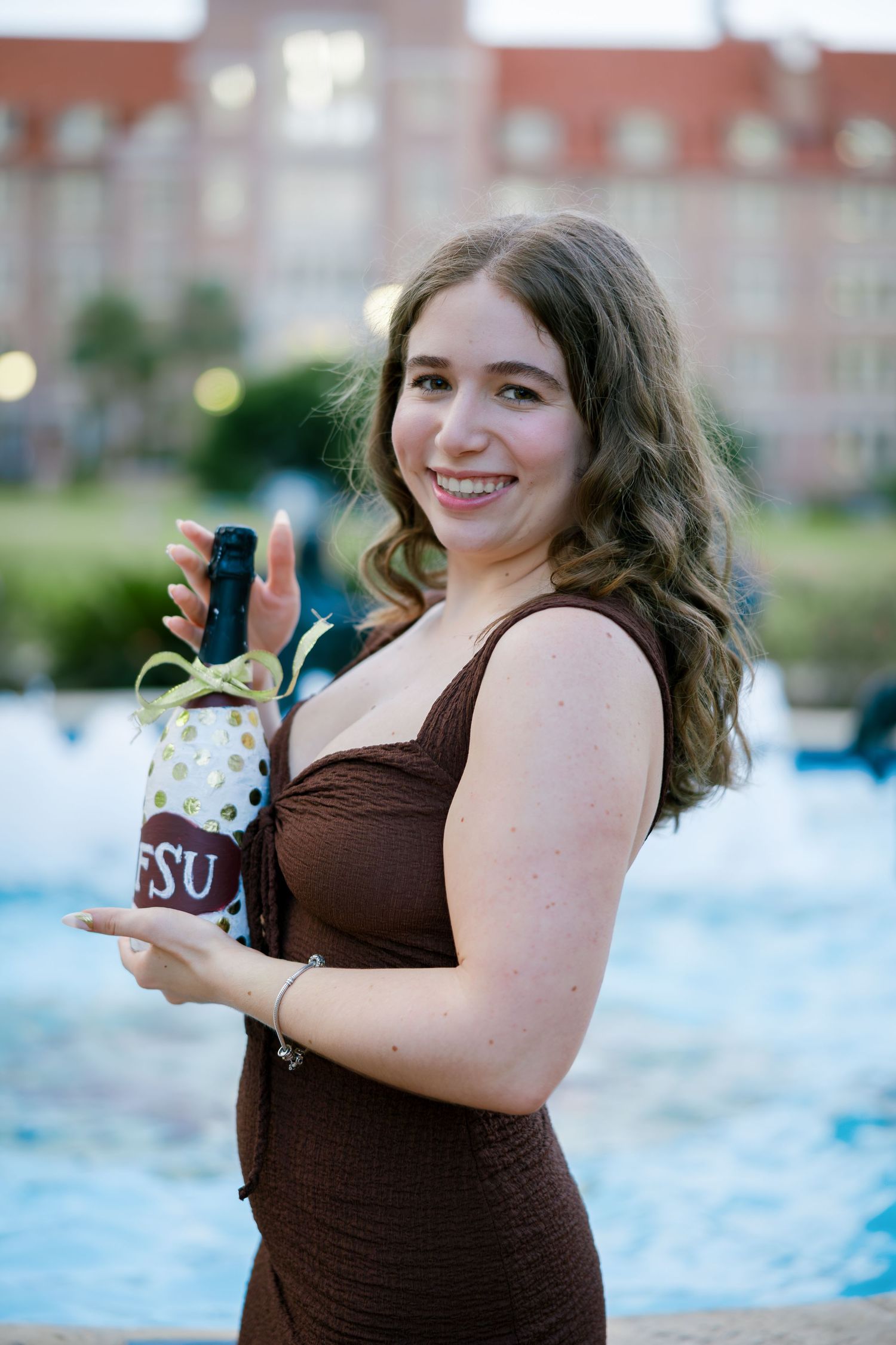 Smiling young woman in brown dress holding an FSU decorated bottle near a fountain on campus.