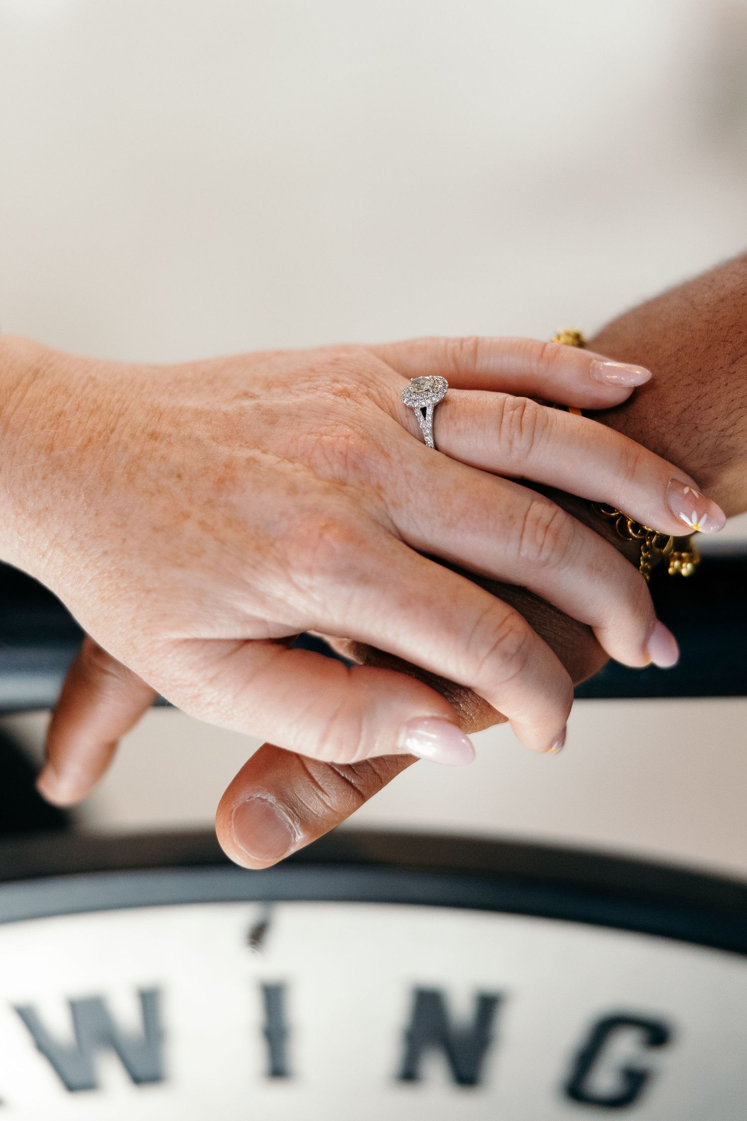 Two hands with different skin tones touching tenderly, with a diamond ring visible on one hand.
