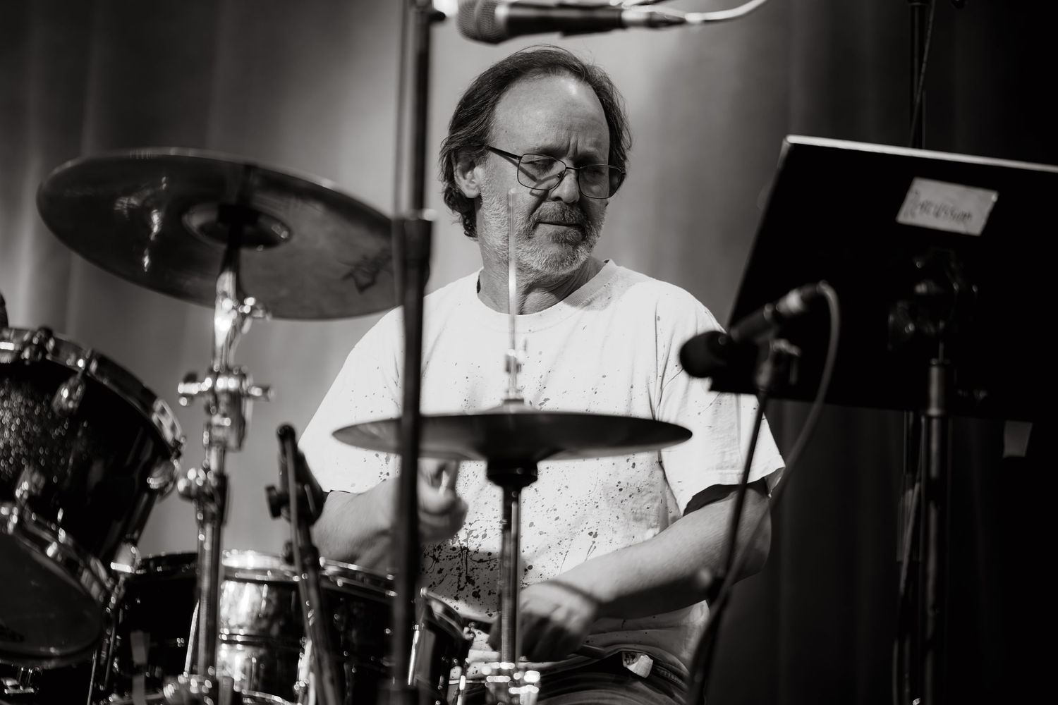 A drummer performs behind a drum kit in a black and white photograph.
