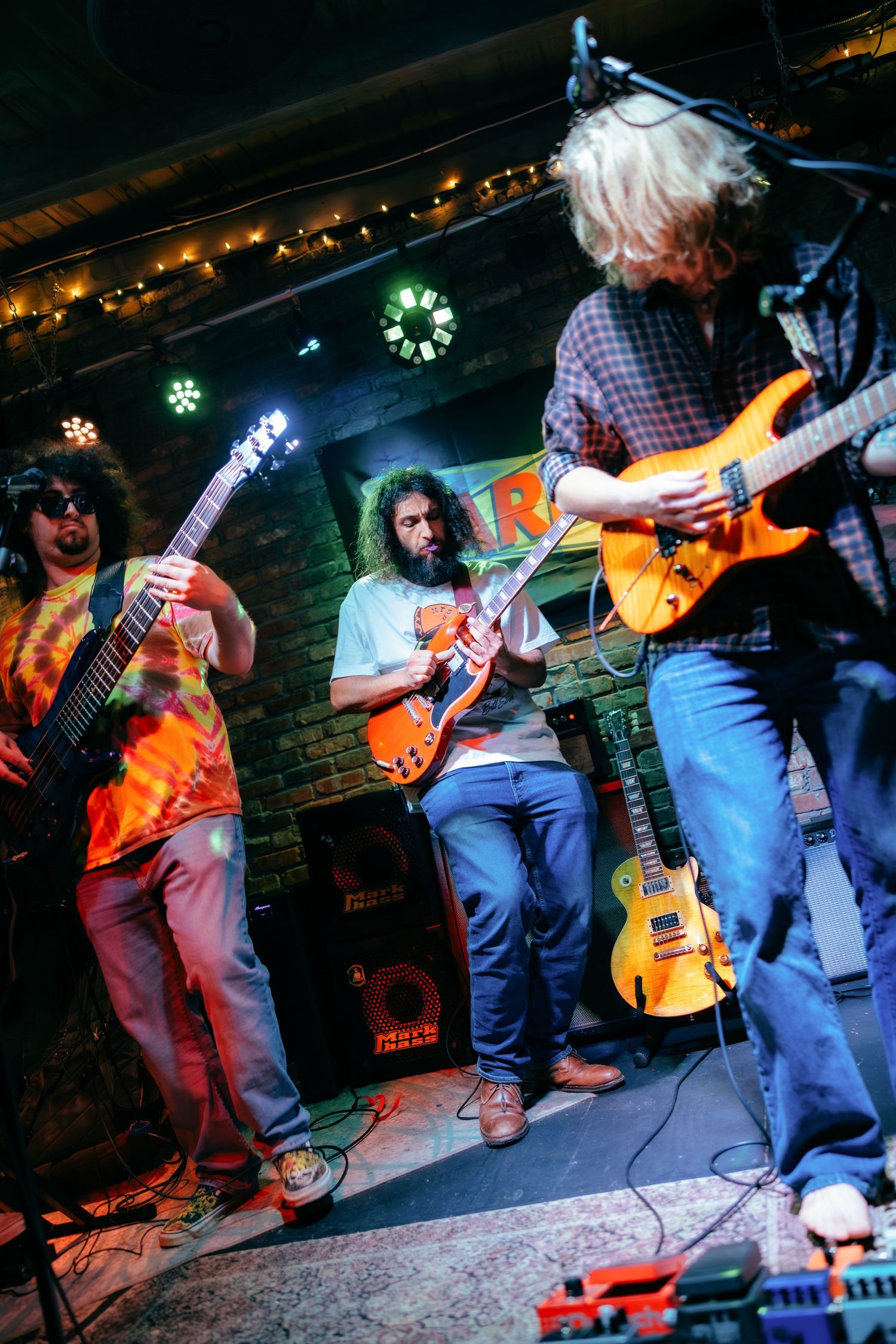 Musicians perform energetically on stage with guitars at a dimly lit rock concert venue.