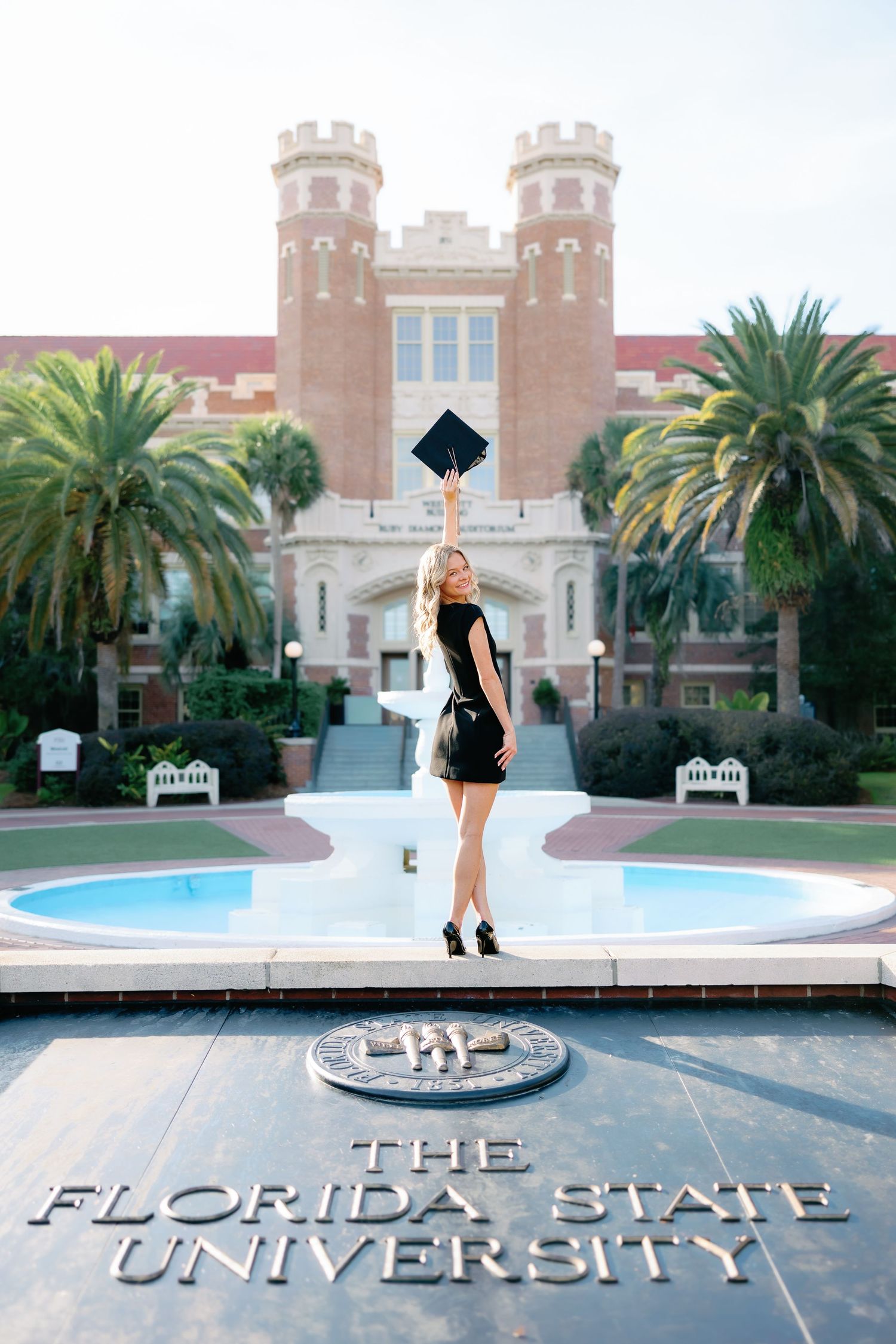 Graduate stands in front of Florida State University's iconic brick entrance with palm trees and fountain.