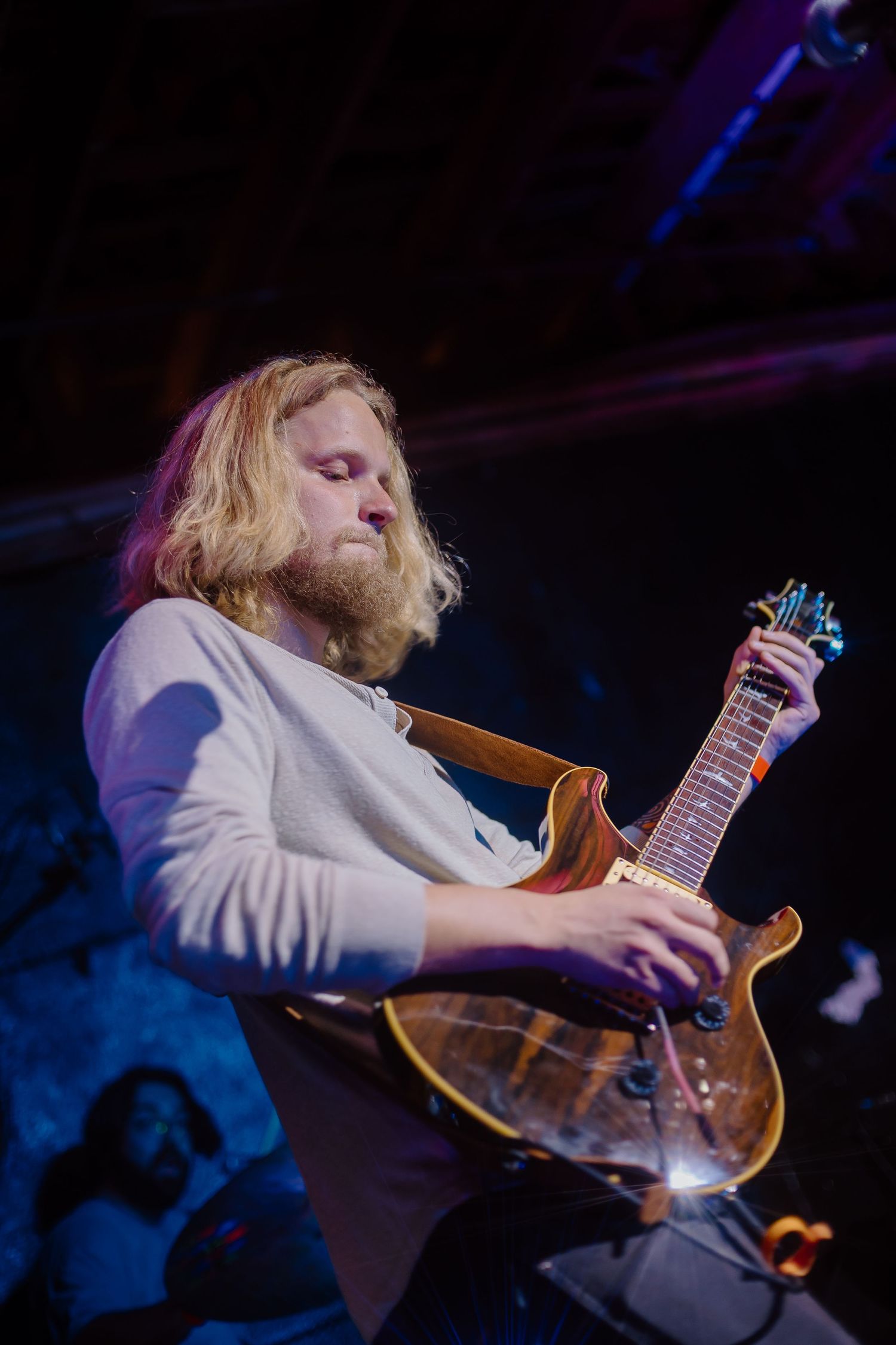 Guitarist performing on stage with dramatic blue lighting while playing electric guitar.
