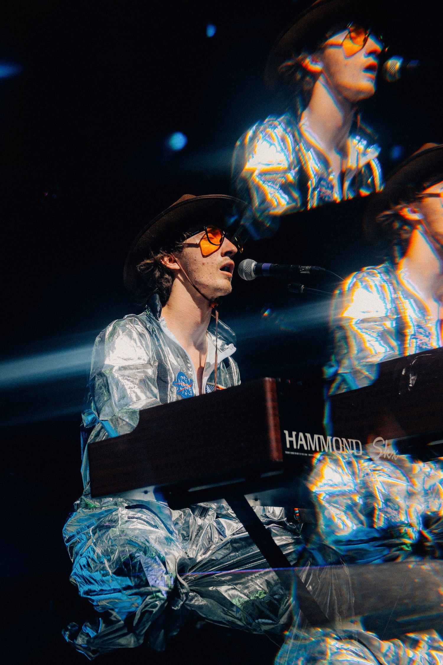 Keyboard player in metallic outfit performs at Hammond organ with dramatic blue stage lighting.