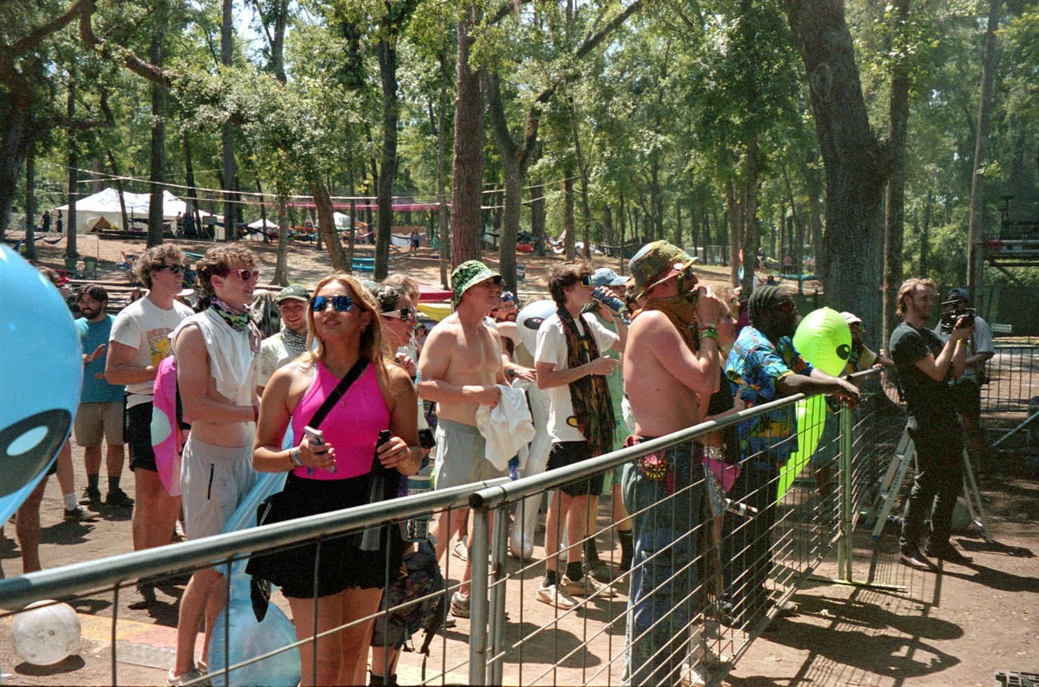 Large crowd of visitors waiting in line along a metal railing in a wooded outdoor area during summer.
