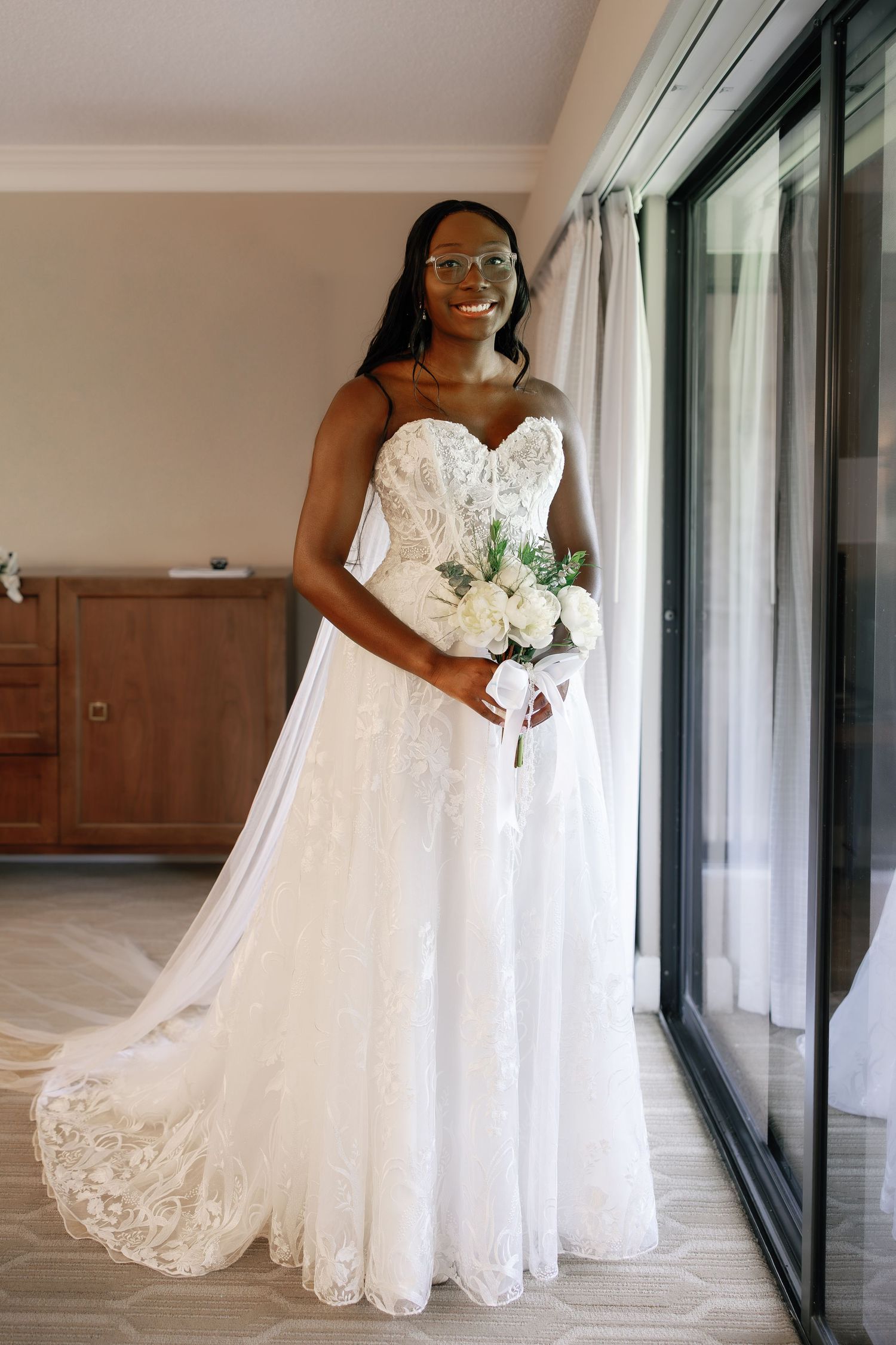 Radiant Black bride in a strapless lace A-line wedding gown holding white roses bouquet indoors.
