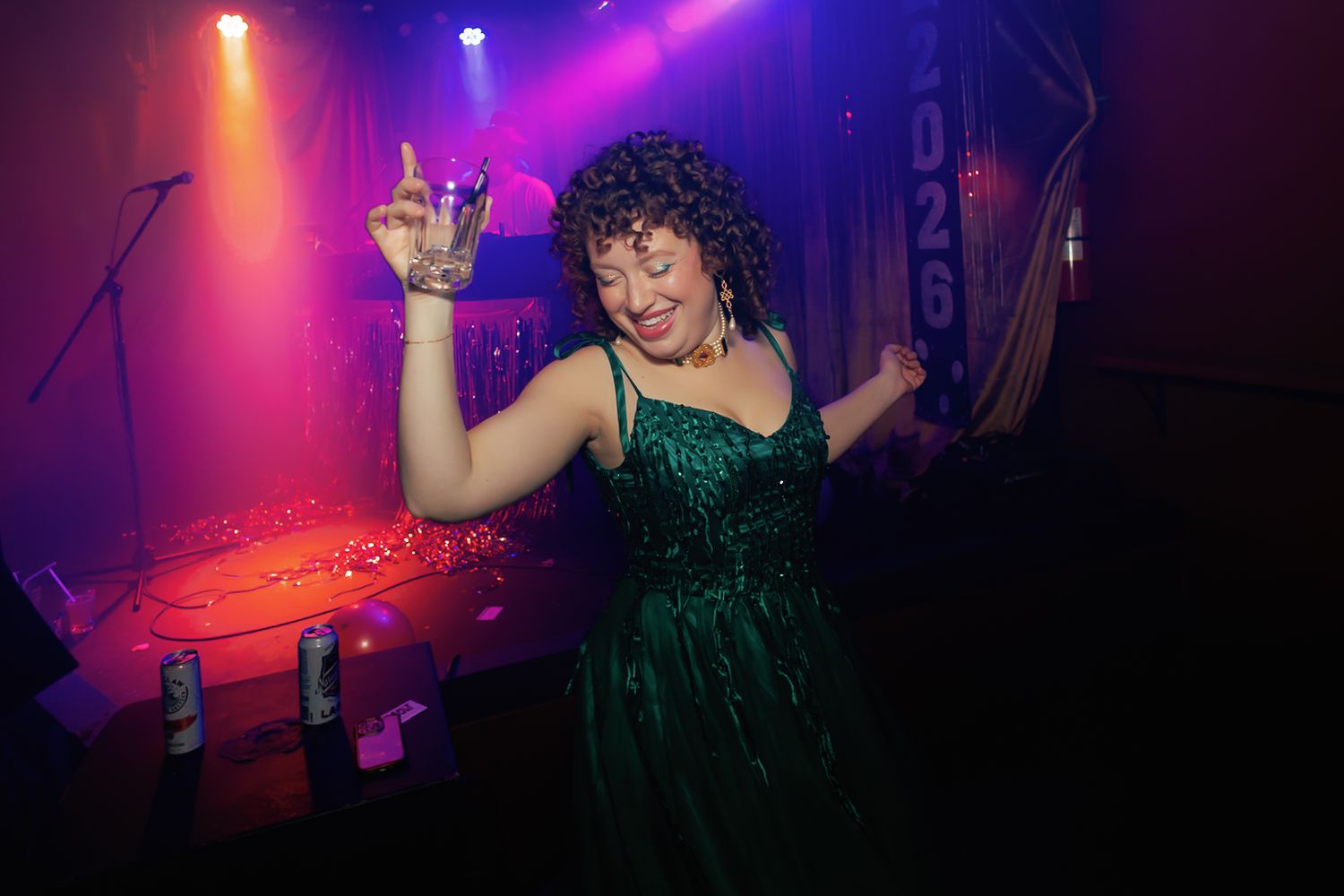 A performer in a green dress dances energetically on stage under vibrant purple and orange concert lighting.