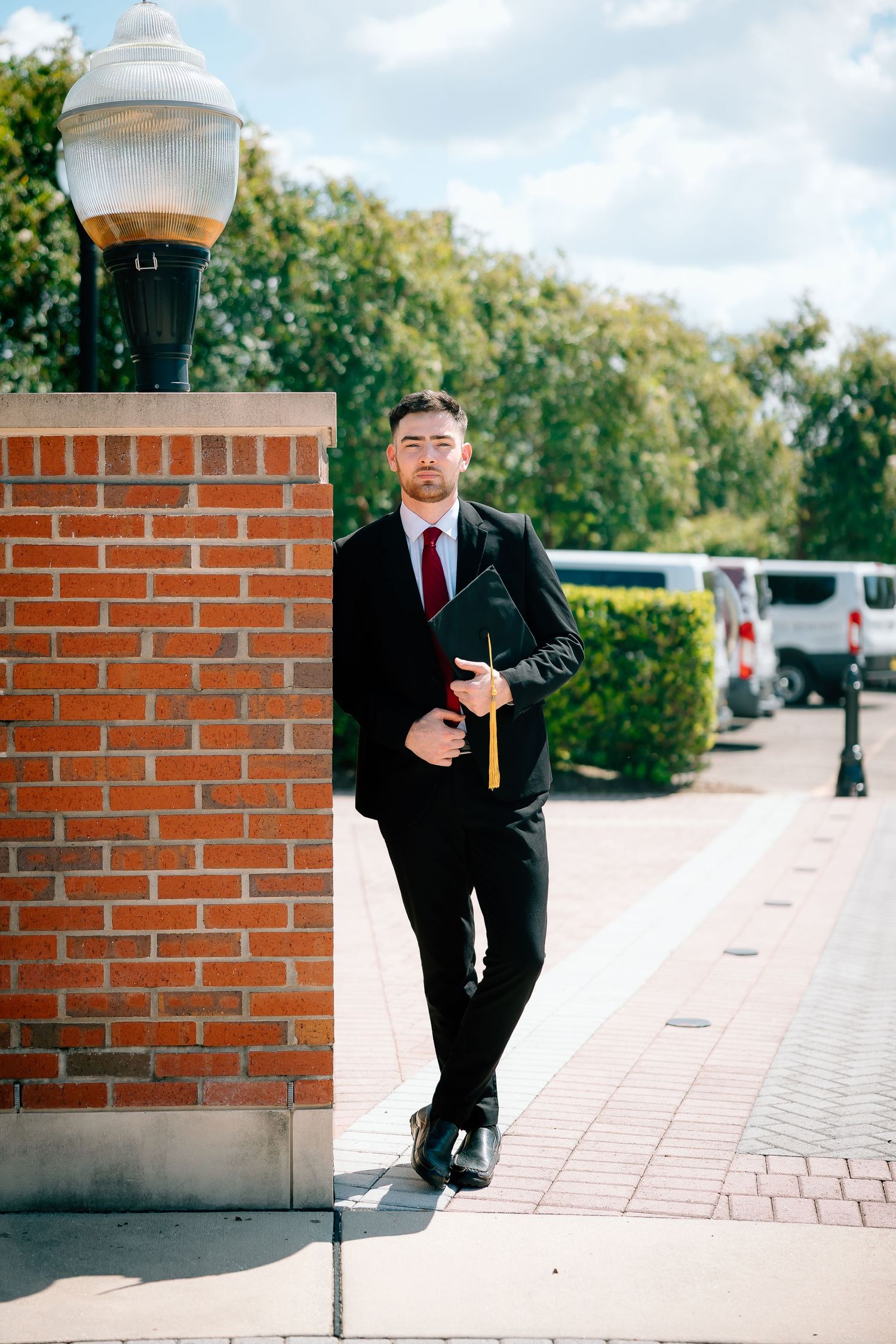 Professional in a black suit poses thoughtfully against a brick wall in an outdoor setting.