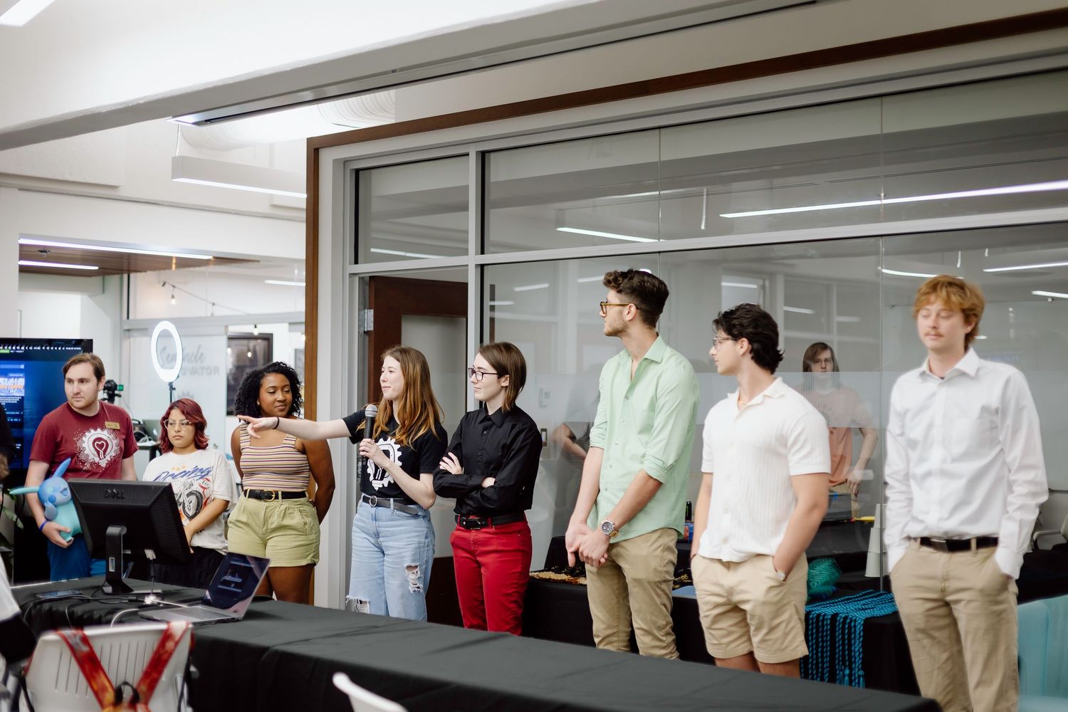 Students gathered in a classroom setting engage in a group discussion while seated at desks and tables.