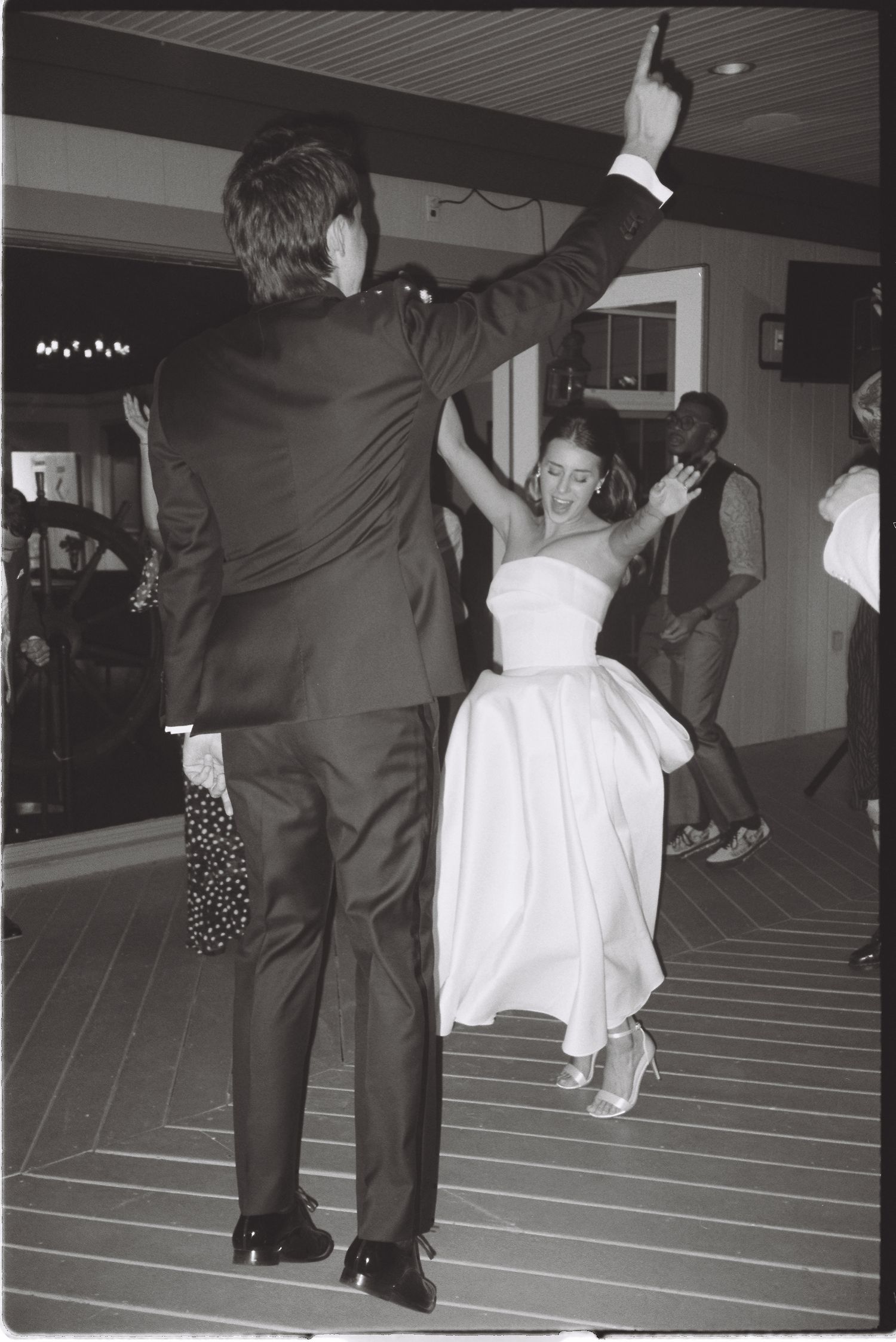 Black and white photo of bride and groom dancing joyfully at wedding reception.