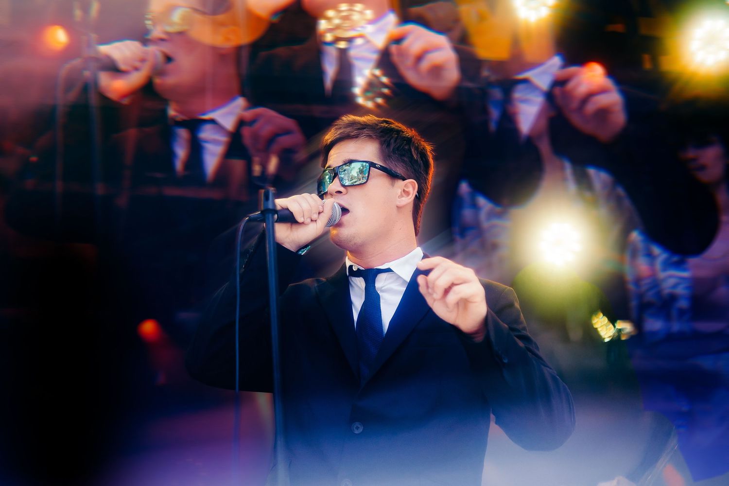 Wedding band performer in navy suit and sunglasses sings into microphone during evening reception performance.