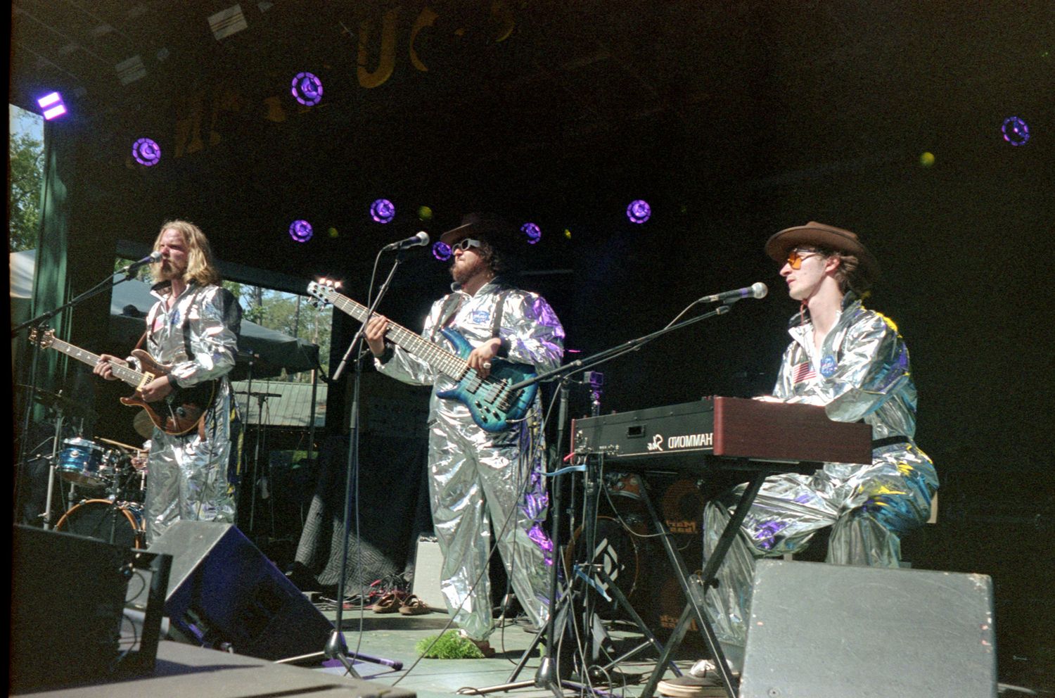 A country band performs on stage in silver clothing with purple lights and musical instruments during a live concert.