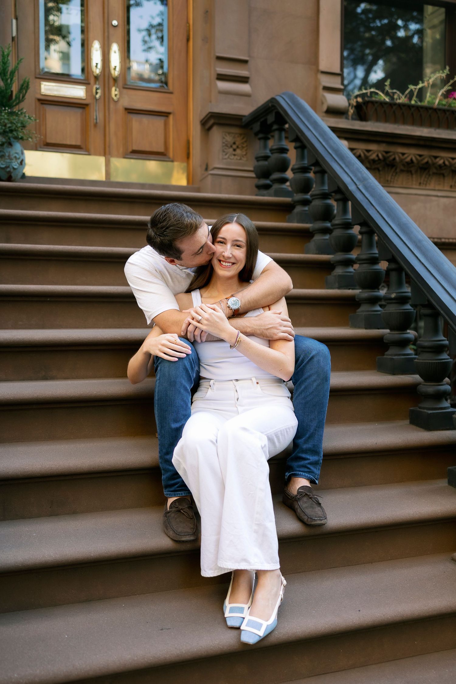 A couple shares a tender moment while sitting on brownstone steps in an urban neighborhood.