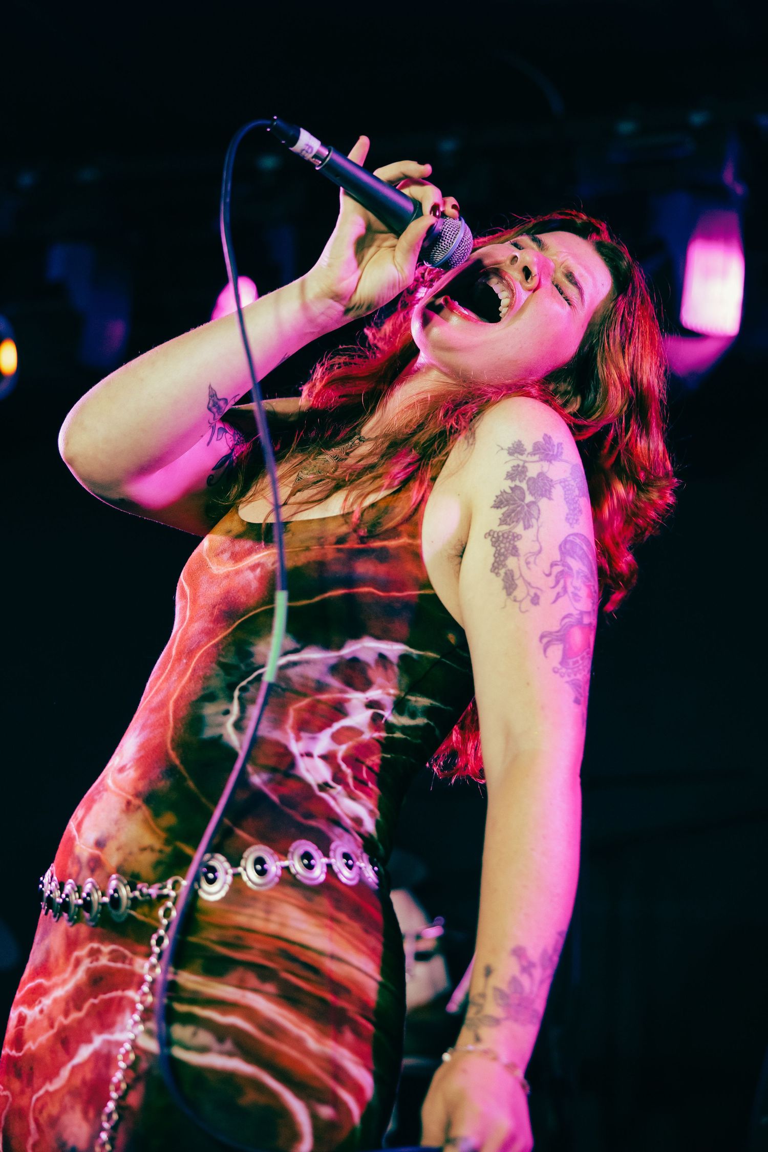 Rock performer in dark lighting sings passionately on stage with dramatic pink and purple lighting effects.