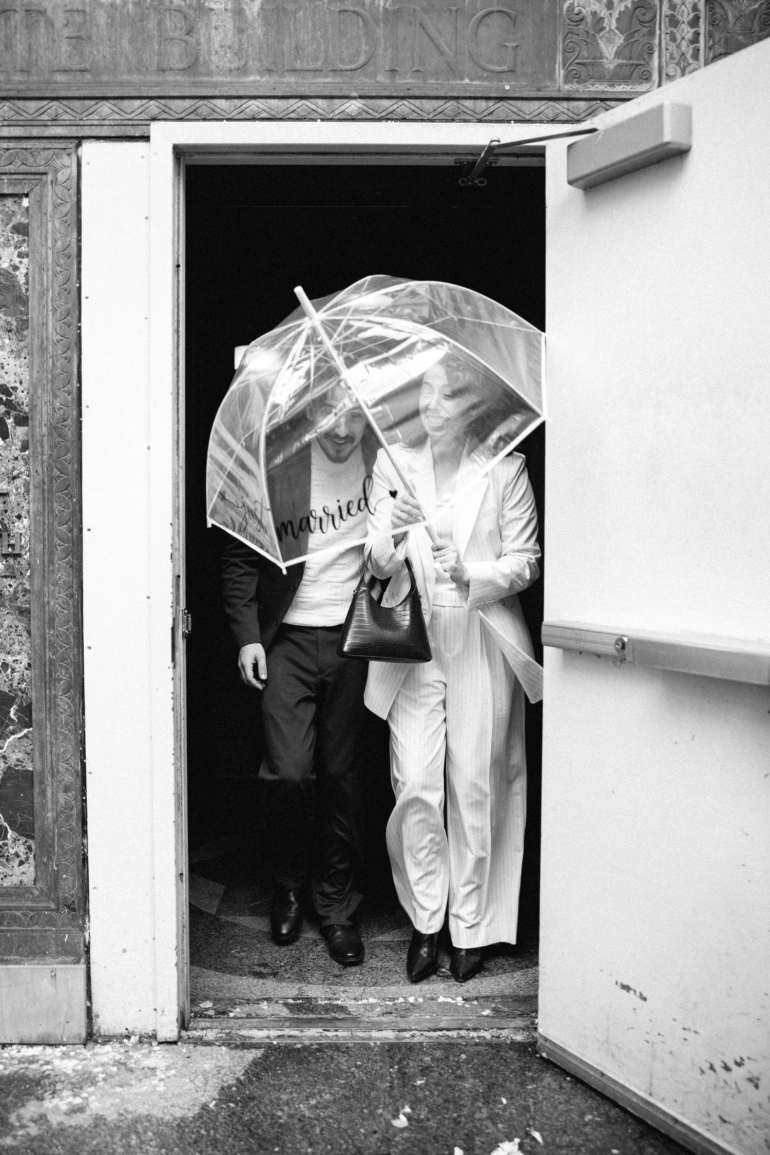 Two figures in white protective suits emerge from a dark doorway in a black and white photograph.