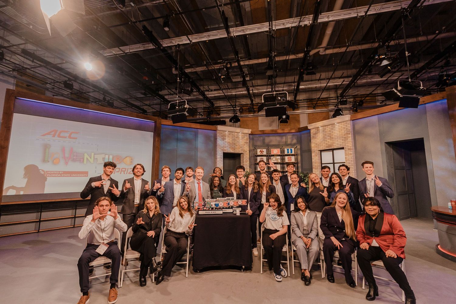 A group photo in a television studio setting with professional lighting and broadcasting equipment visible in the background.
