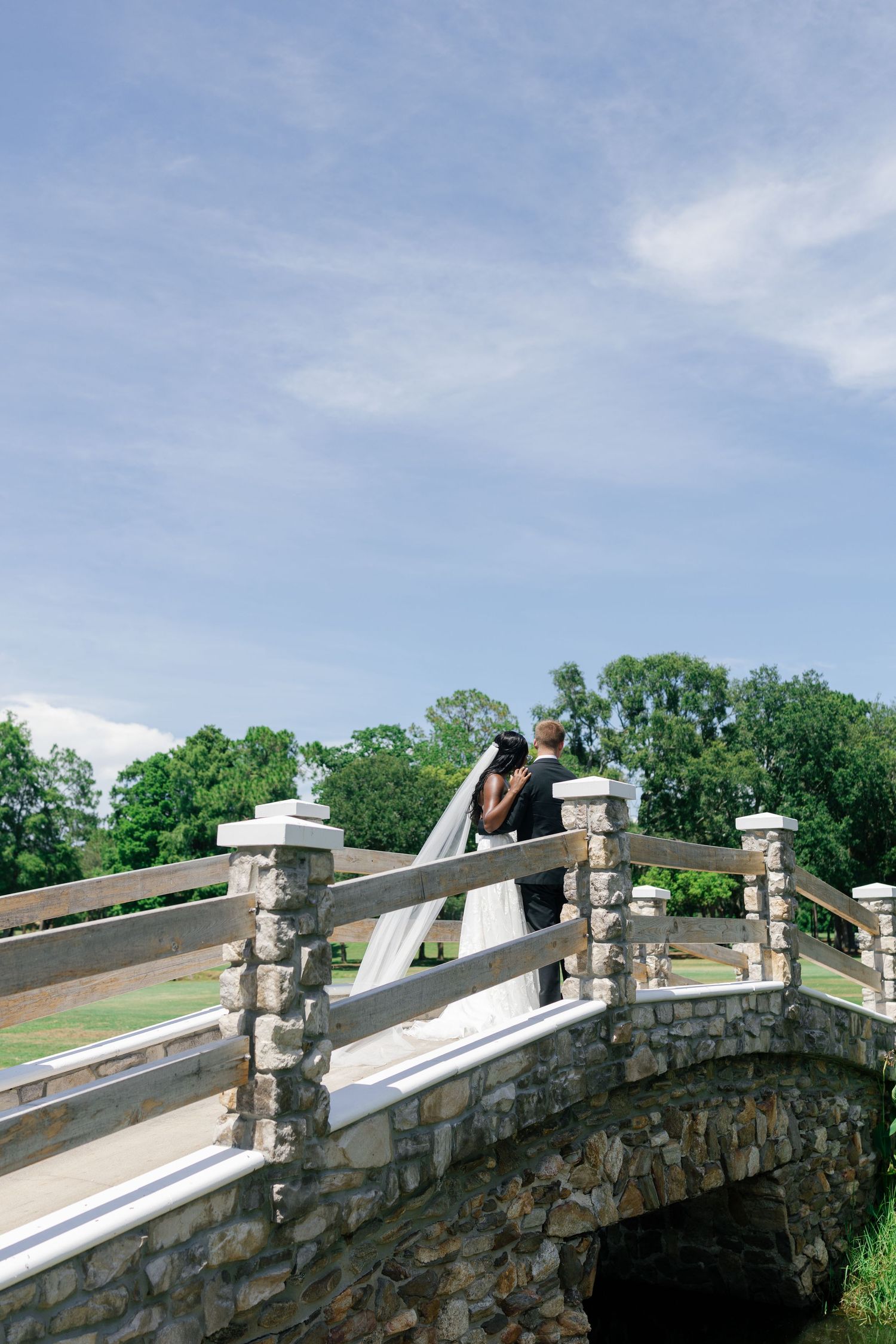 Bride and groom sharing romantic moment on stone arch bridge at outdoor wedding.