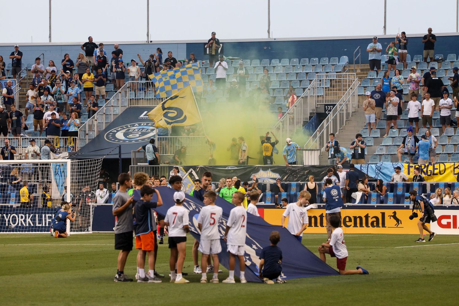 MLS Philadelphia Union soccer fans celebrate in stadium bleachers with yellow smoke flares during a match at a sporting event.