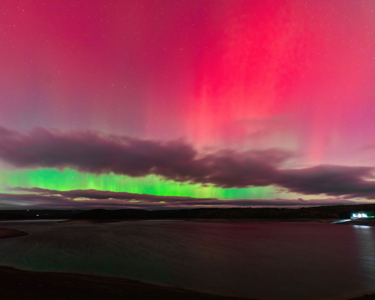 Spectacular pink and green aurora borealis lights dance across the night sky over a dark coastline and water in New York State.