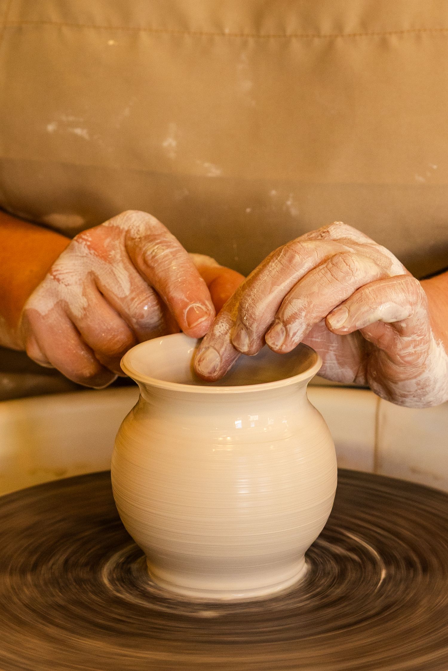 Hands shaping a clay pot on the pottery wheel at Amfora Studio