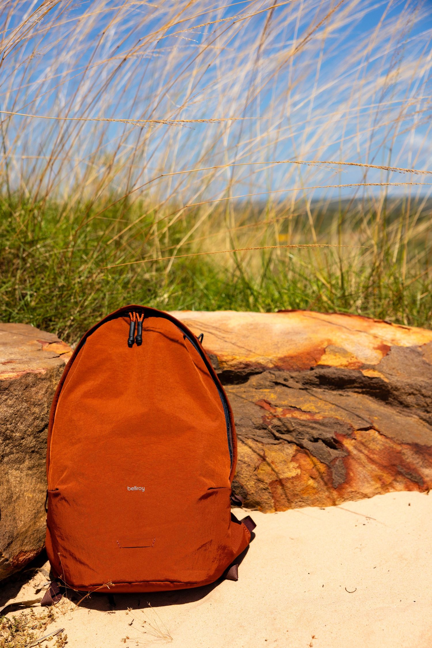 Rust Bellroy backpack resting on a log among coastal grasses, Kimberley