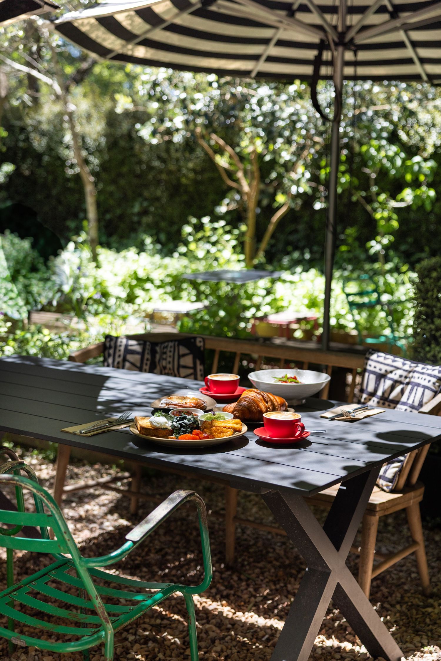 Garden table set with brunch under a striped umbrella at Wombat Hill House Cafe