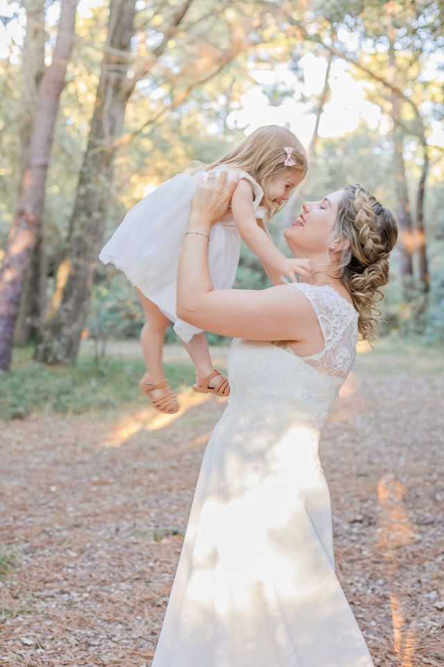 A tender moment between a mother in a wedding dress and small child in a wooded setting.