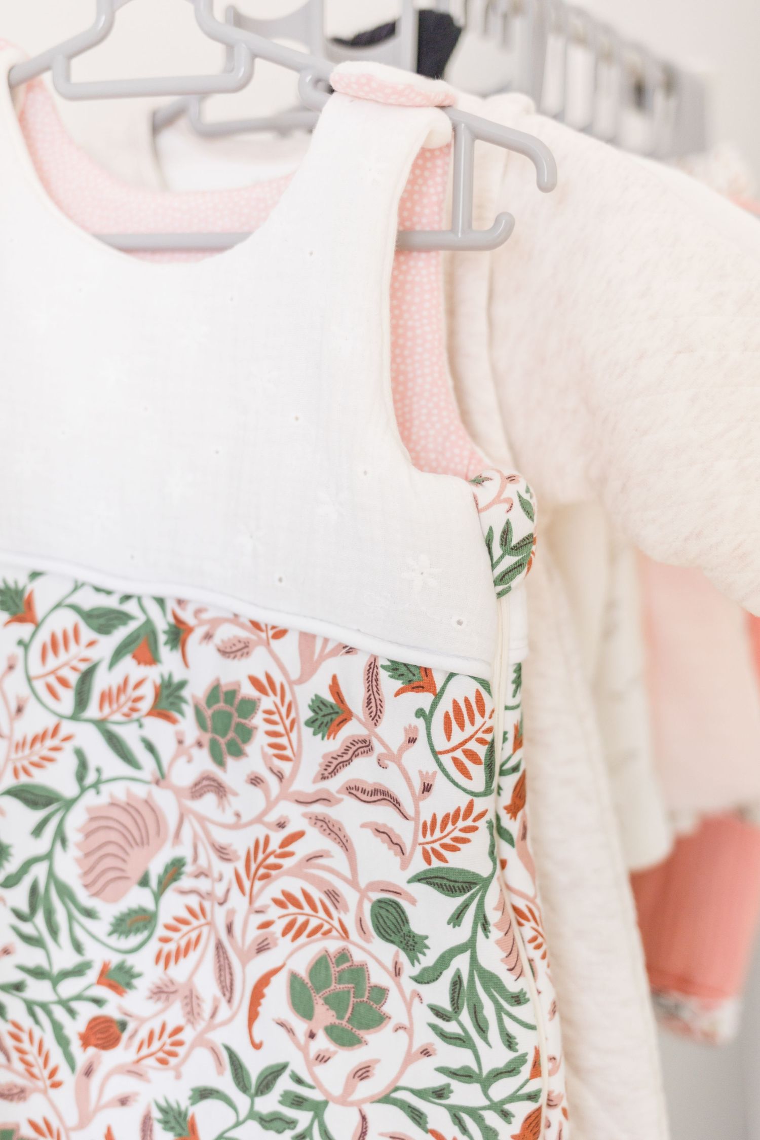 Close-up of baby clothes featuring floral print fabric in pink and white hanging on white hangers.