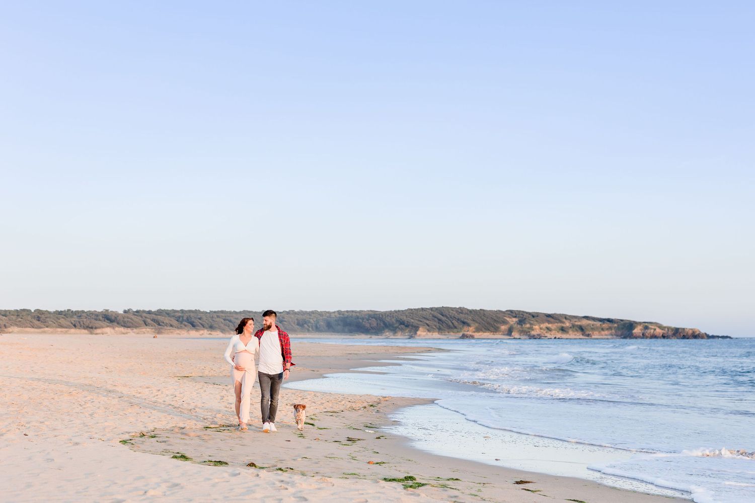 Panoramic view of a coastal beach with cliffs and distant figures on the sand.