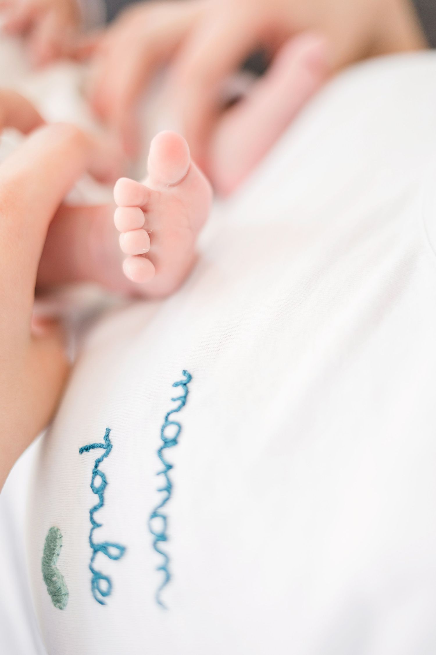 Macro shot of baby feet with embroidered text on white clothing.