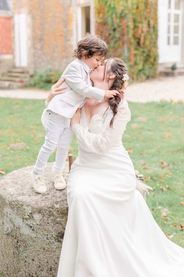 An intimate wedding portrait taken outdoors by a stone wall with autumn foliage in the background.