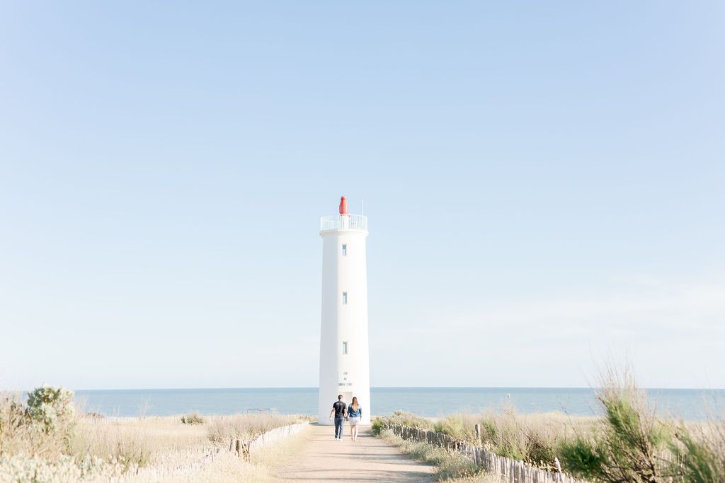Minimalist view of white lighthouse on coastal landscape under bright blue sky.