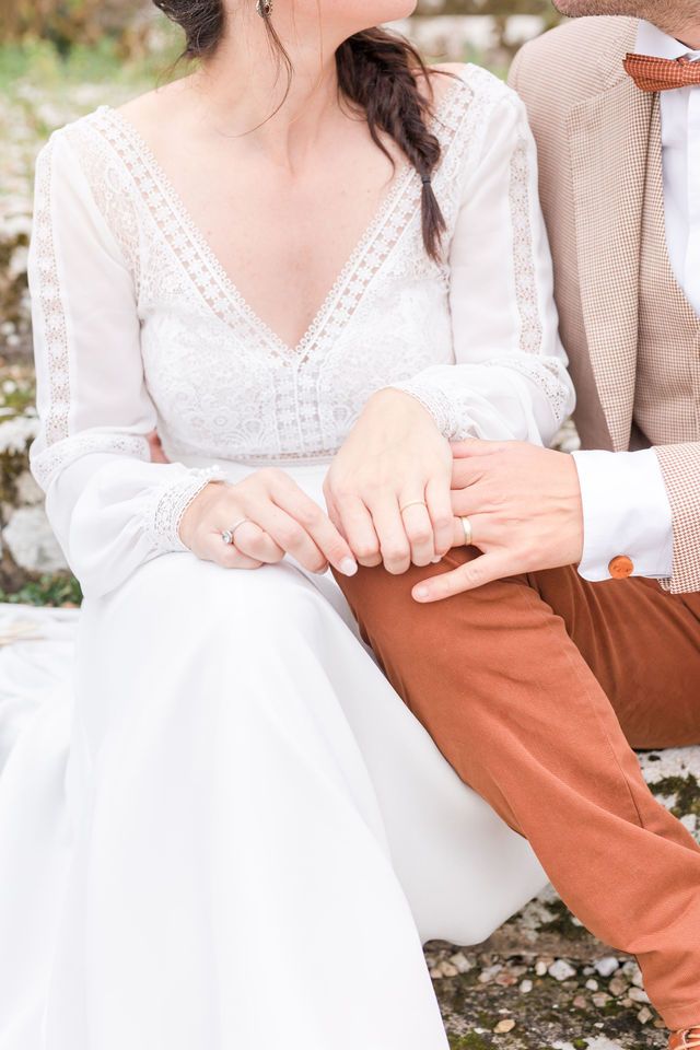 Detail shot of wedding dress lace and hands against rust-colored pants.